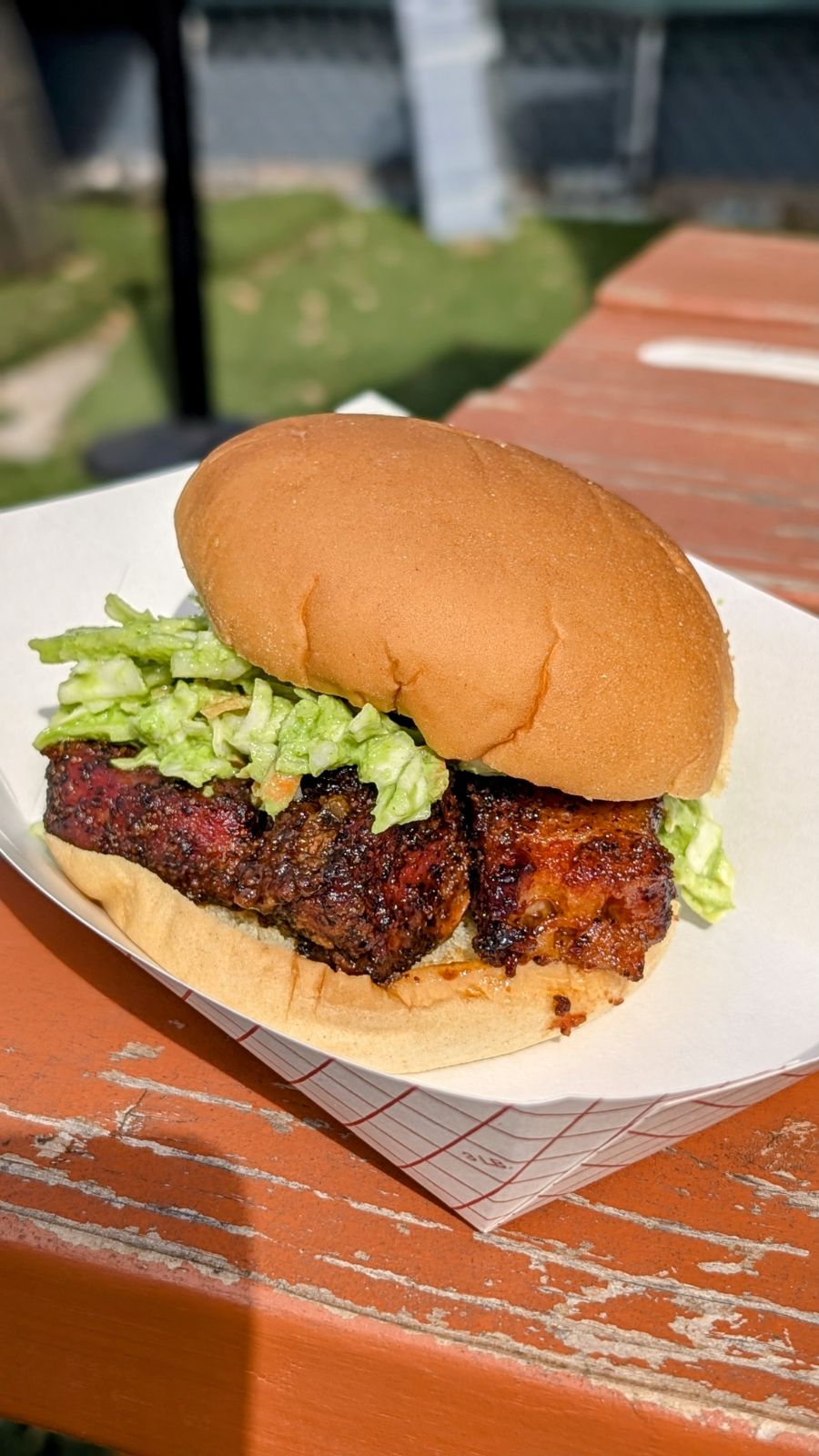 Glazed meat and coleslaw sandwich in a paper tray.