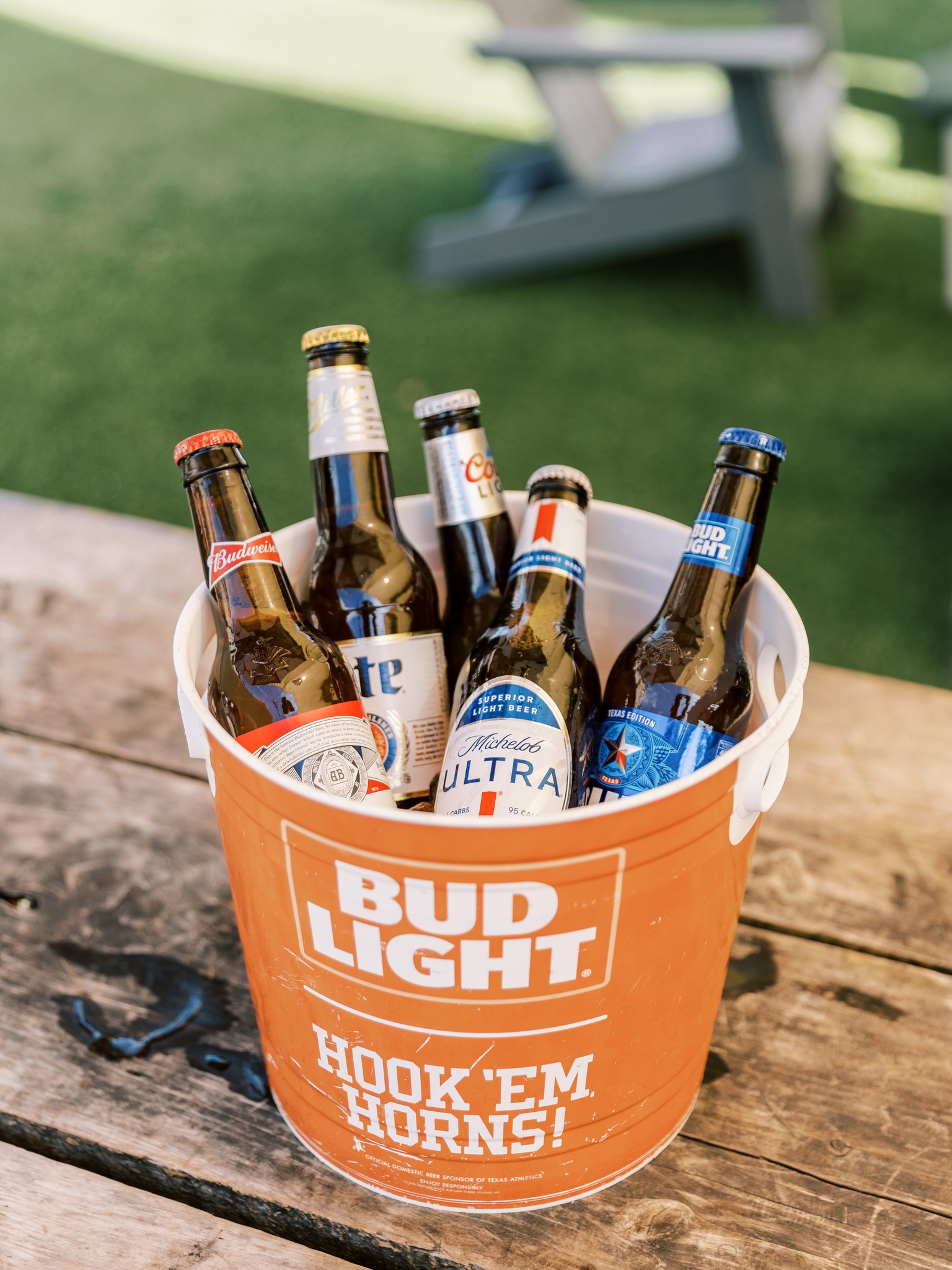 Orange Bud Light bucket filled with various beer bottles on wooden table.