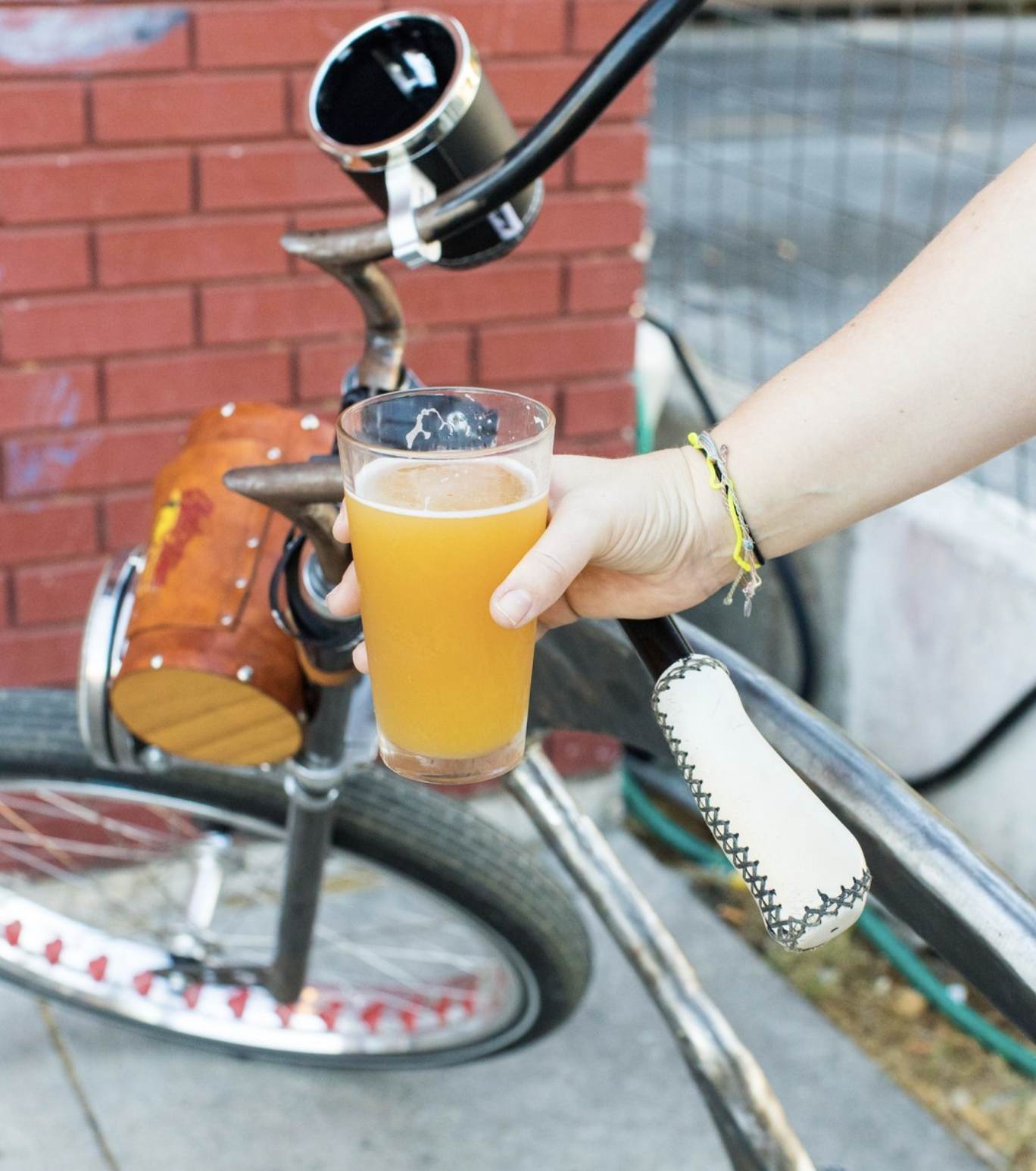 Hand holding glass of foamy, amber beverage next to bicycle.