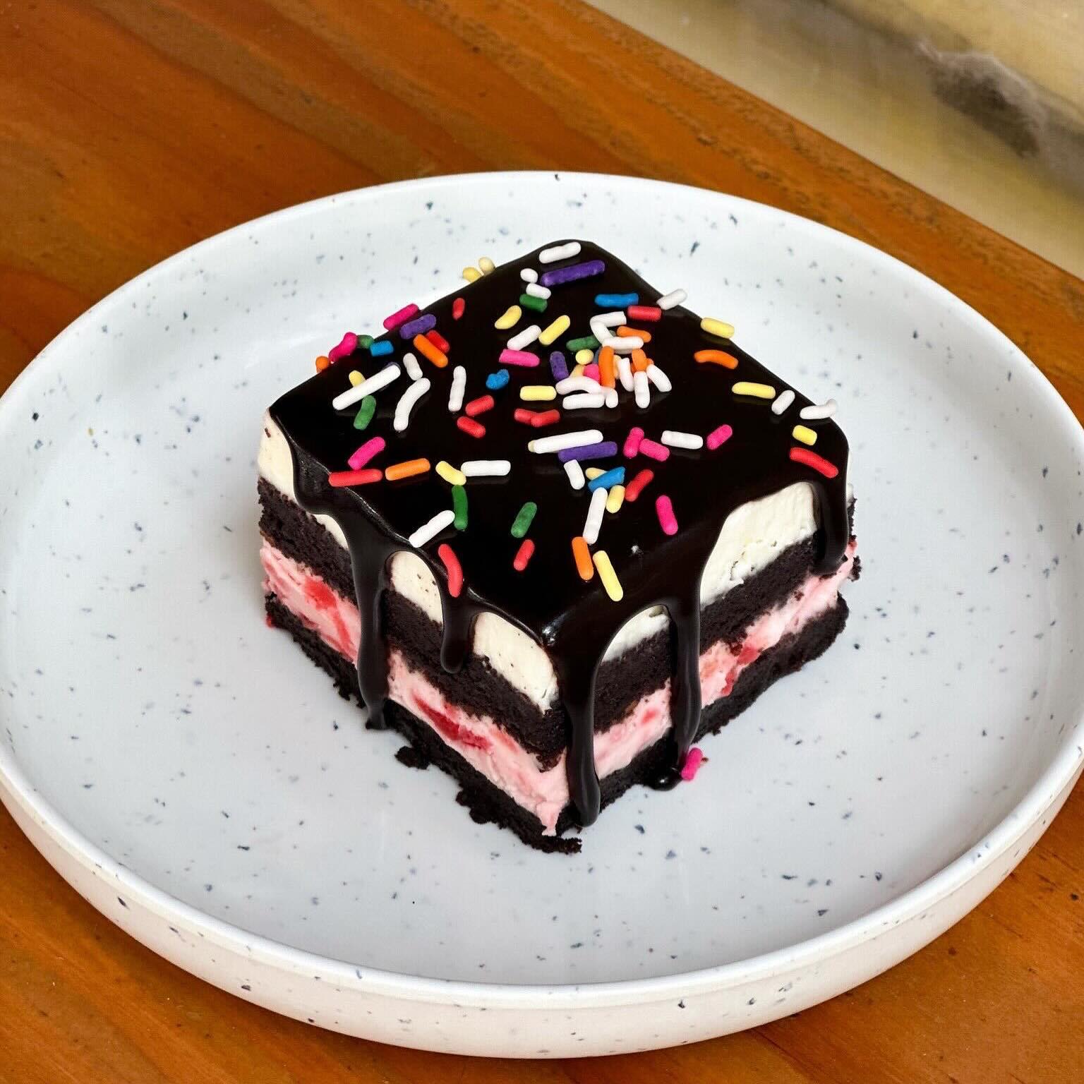 Chocolate cake with white and pink layers, chocolate glaze, and colorful sprinkles.