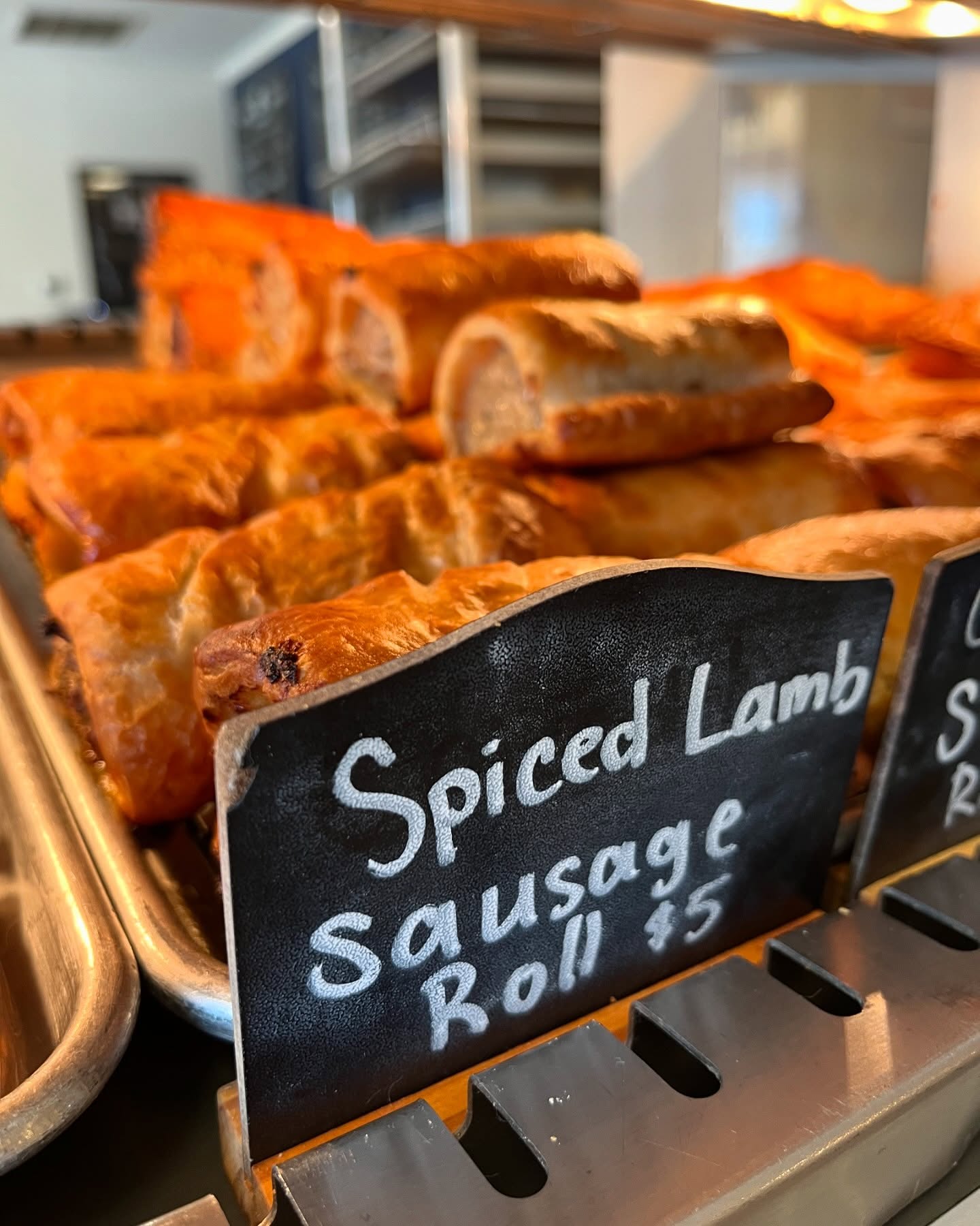 Spiced lamb sausage rolls displayed with a price sign in a bakery.