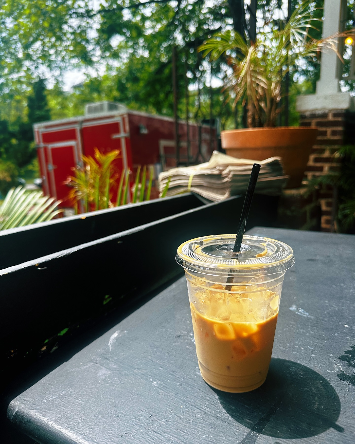 Iced coffee in a clear cup with straw on outdoor table.