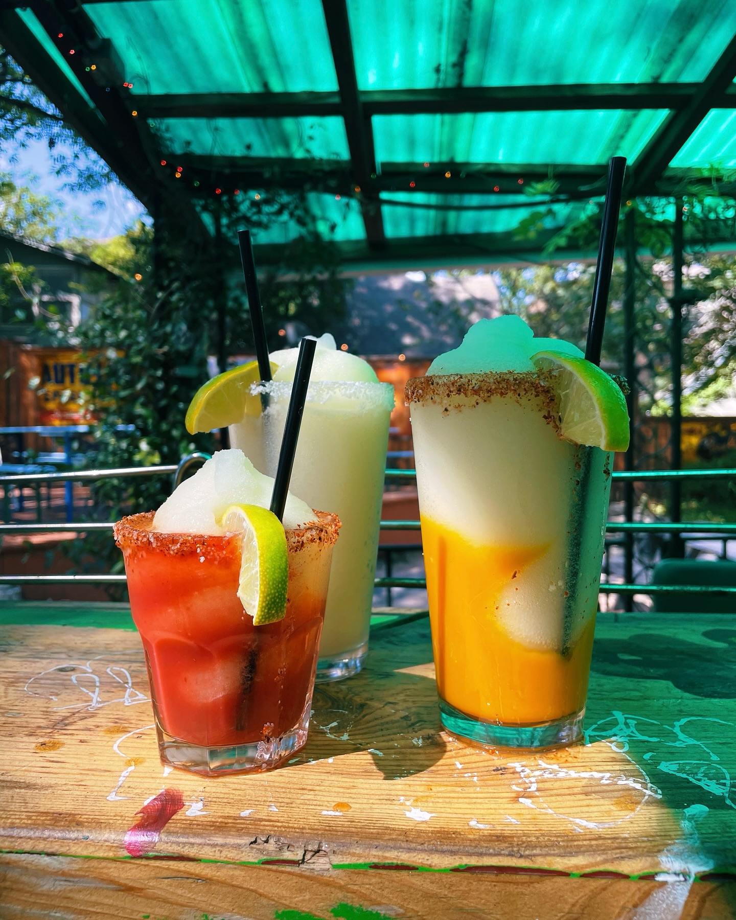 Three frozen drinks with lime wedges and straws on a wooden table.