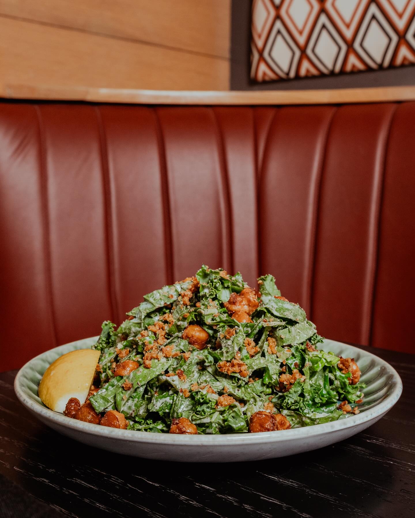 Leafy green salad with dressing, brown pieces, lemon, red booth.