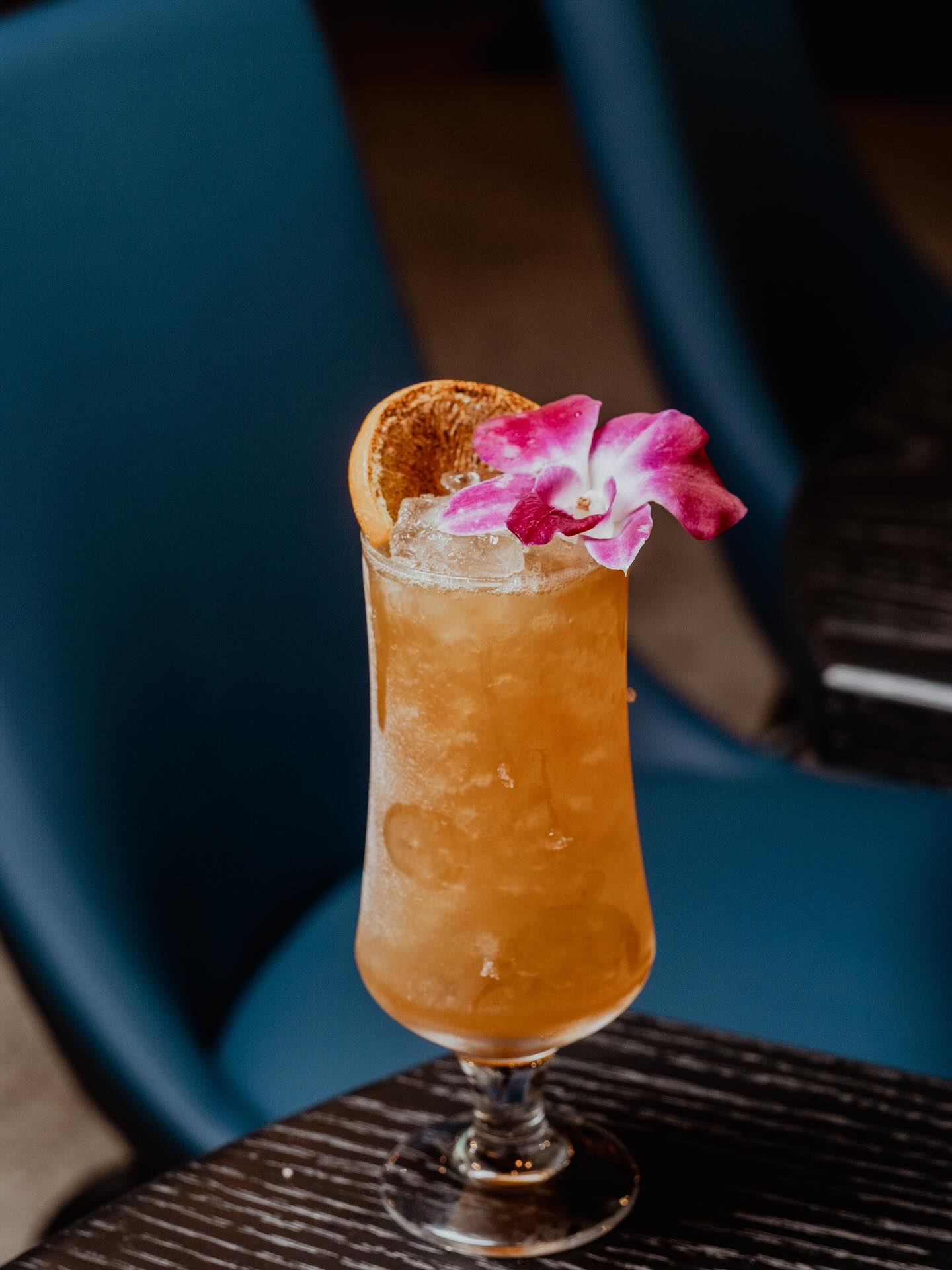 Iced cocktail with orange slice and pink orchid on dark table.
