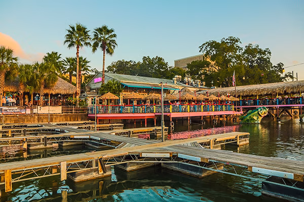 Colorful waterfront restaurant with boat docks and palm trees.