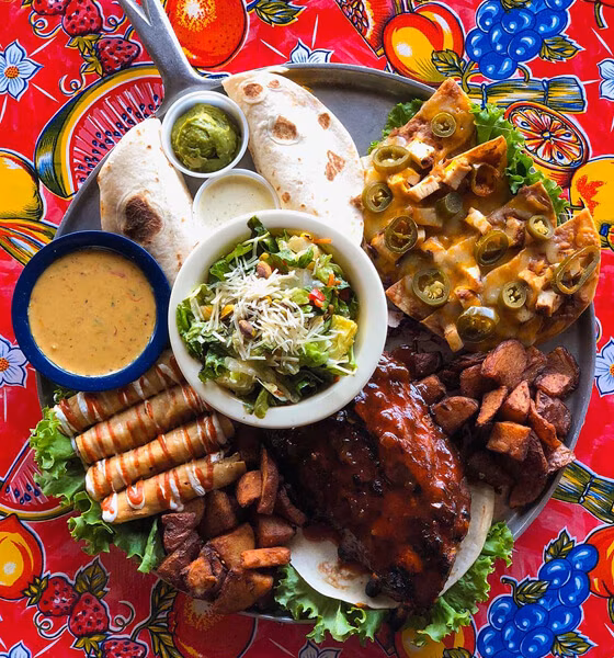 Large platter of nachos, ribs, taquitos, salad, and various sides.