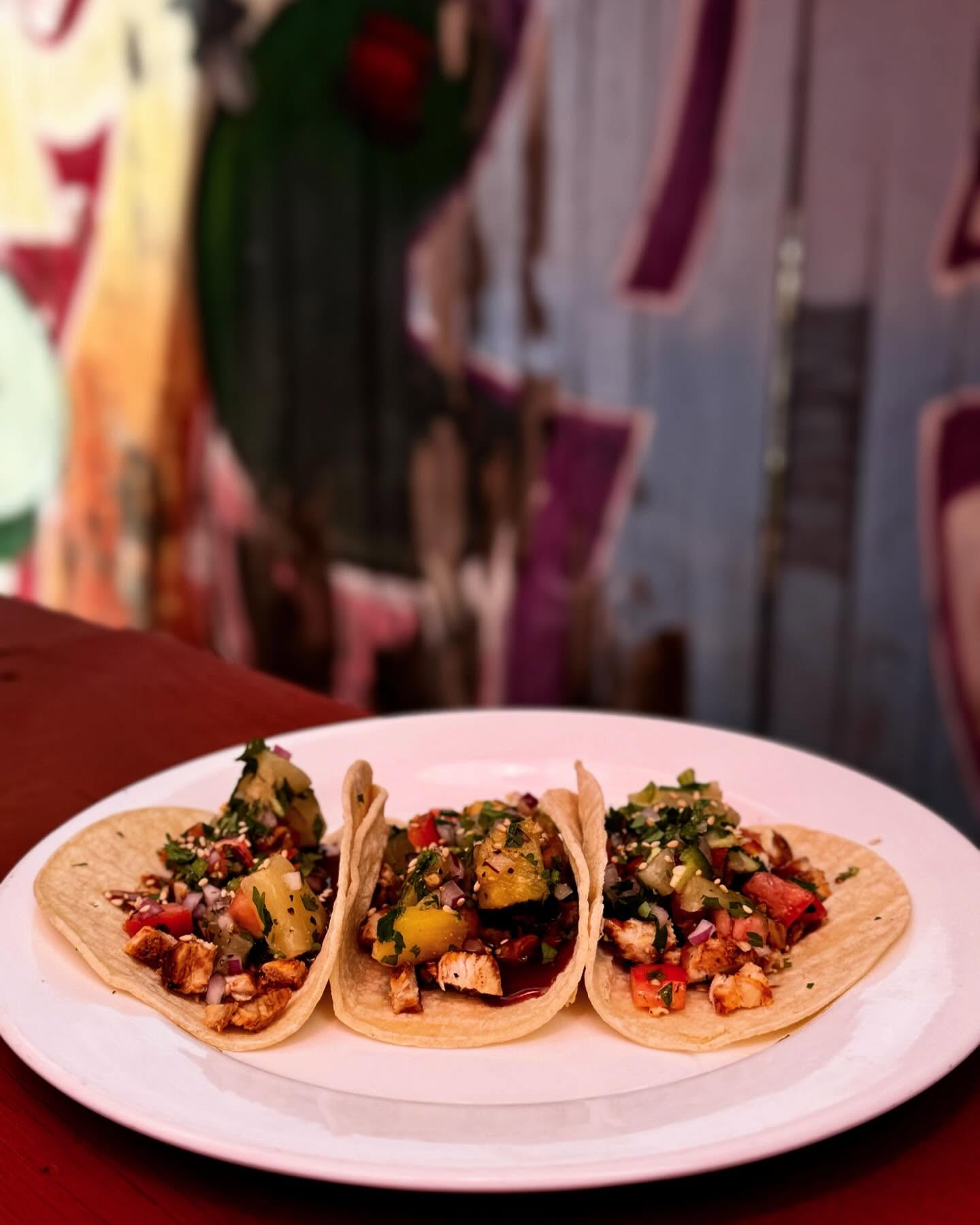 Three small chicken tacos with pineapple and cilantro on a white plate.