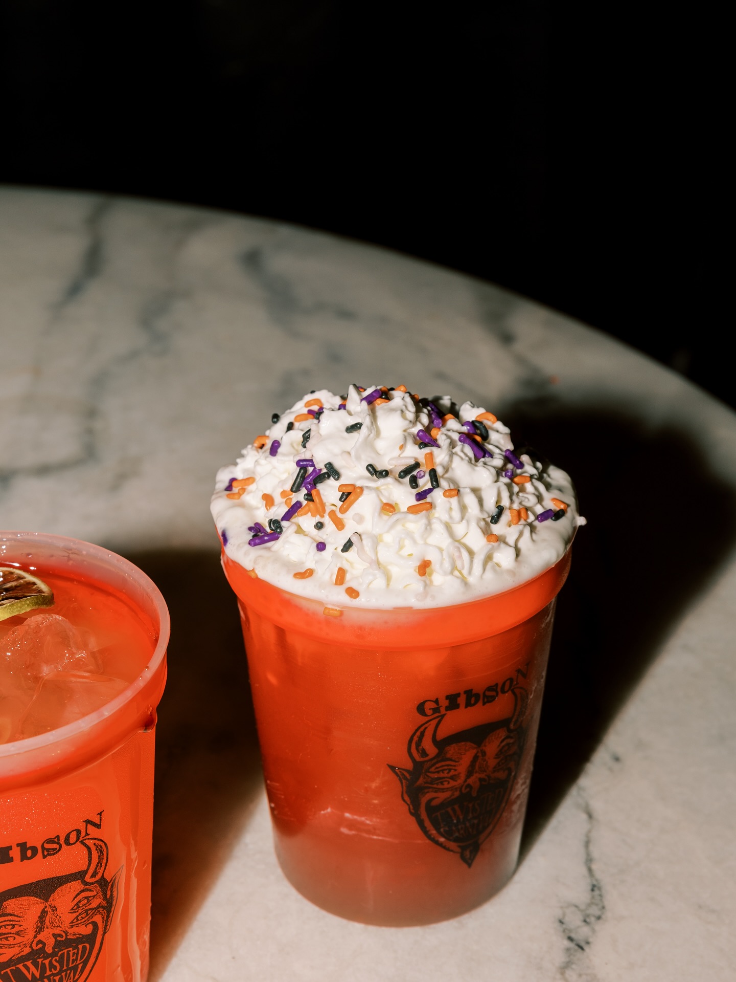 Halloween-themed drink in orange cup with whipped cream and sprinkles.