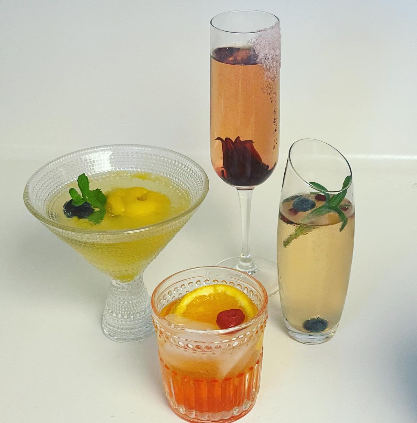 Four colorful cocktails in different glasses with various fruit garnishes.