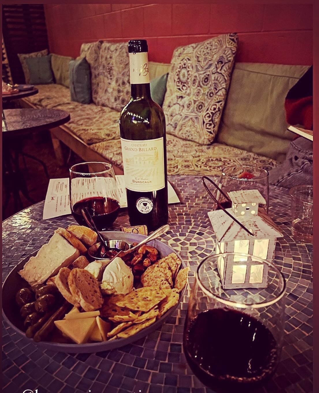 Red wine bottle, glasses, and charcuterie board on a mosaic table.