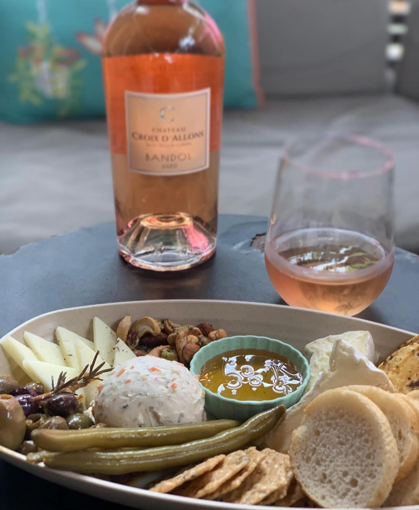 Rosé wine bottle, glass, and a diverse platter of cheeses and snacks.
