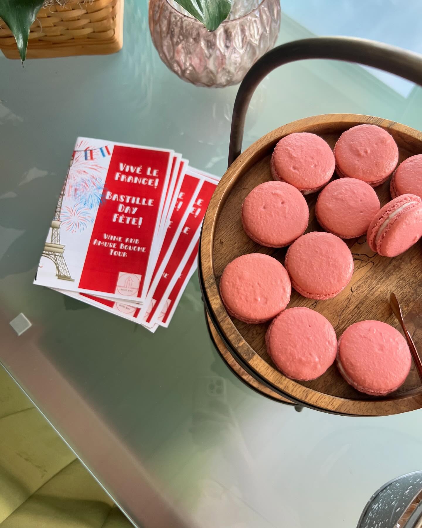 Pink macarons in a wooden tray next to Bastille Day brochures.