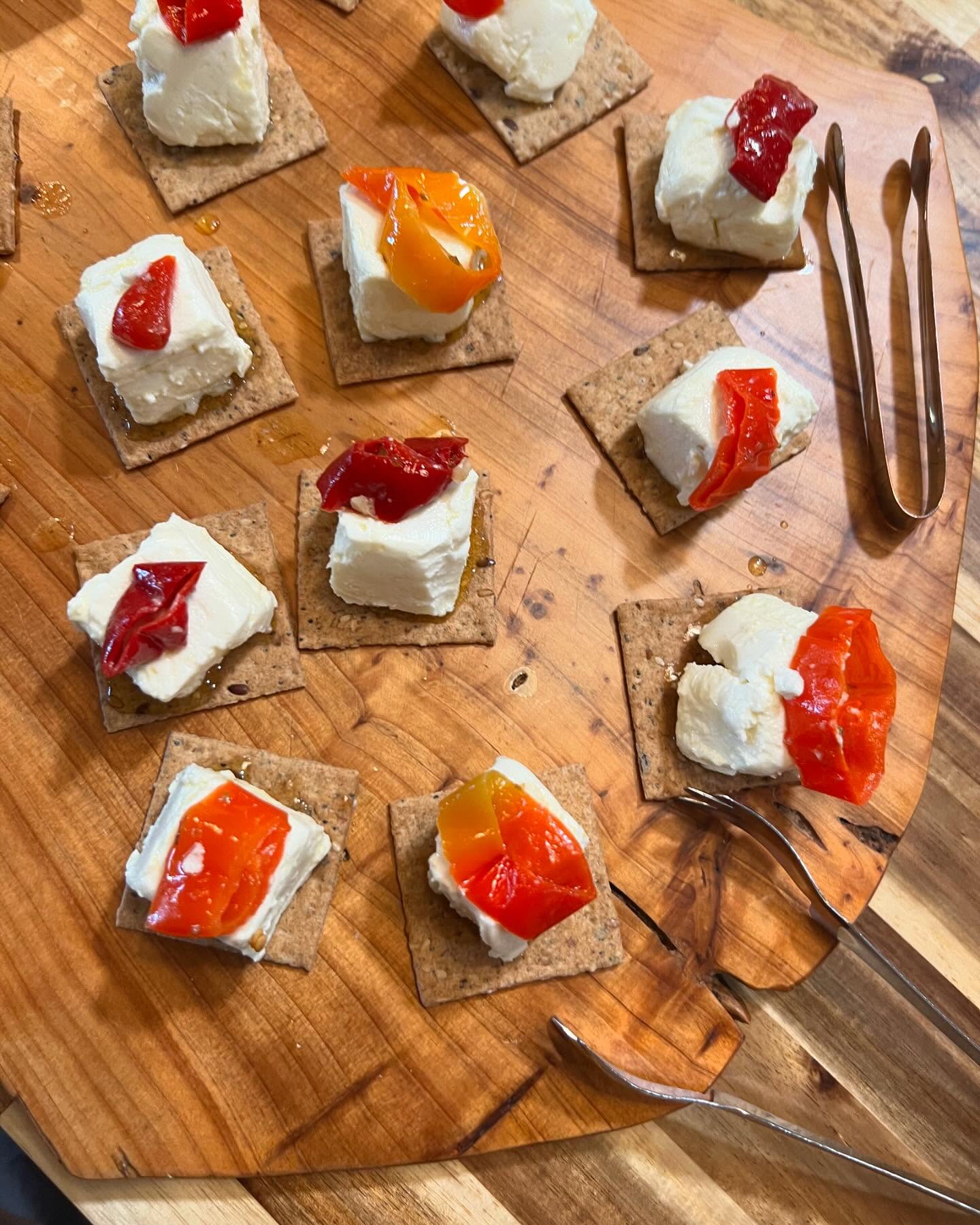 Crackers topped with white cheese and colorful peppers on a wooden board.