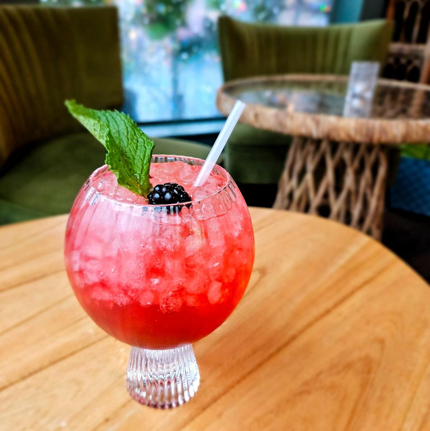 Red drink with blackberry, mint, and ice on a wooden table.