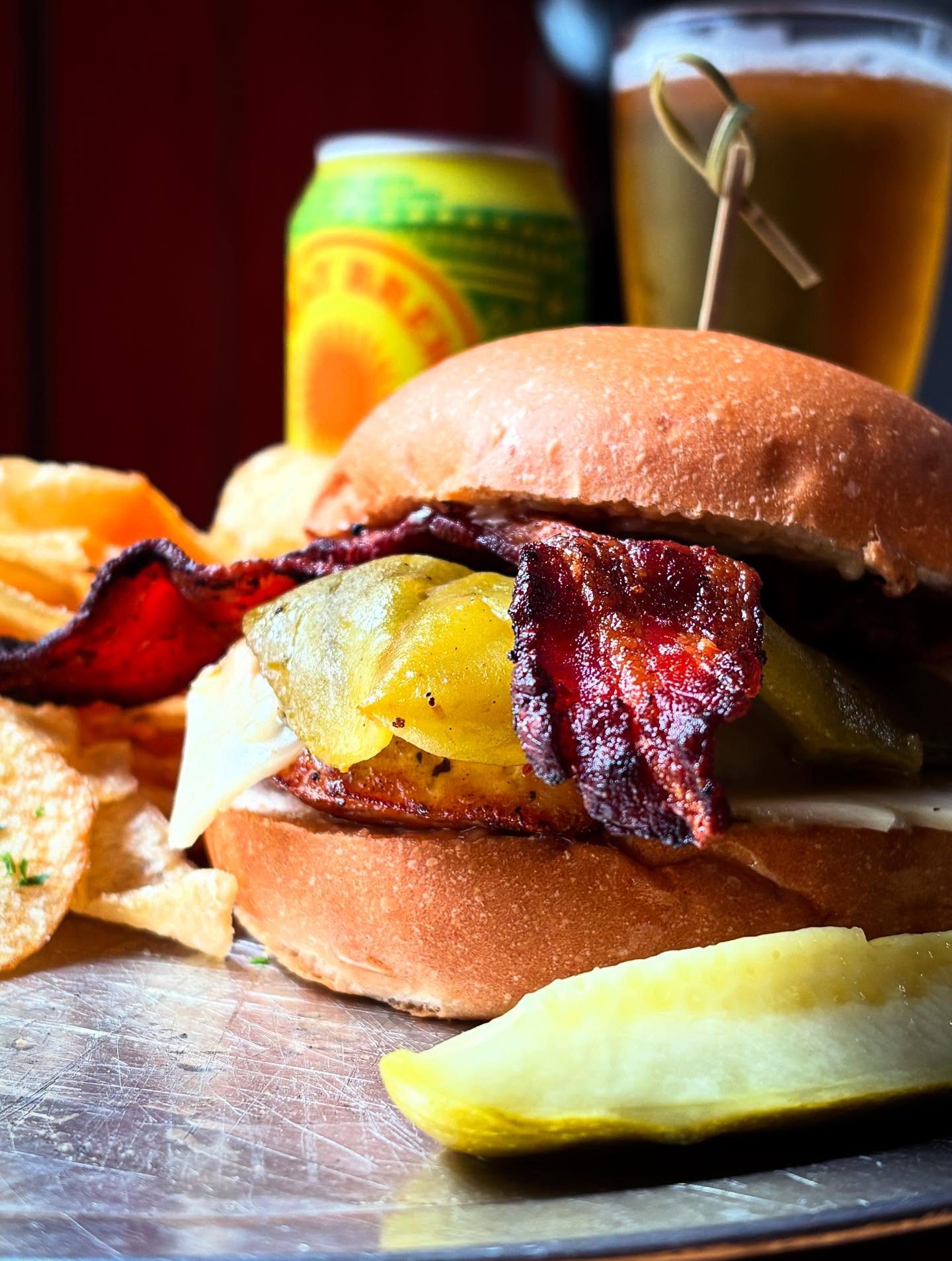 Burger with bacon, peppers, cheese, chips, pickle, and beer.