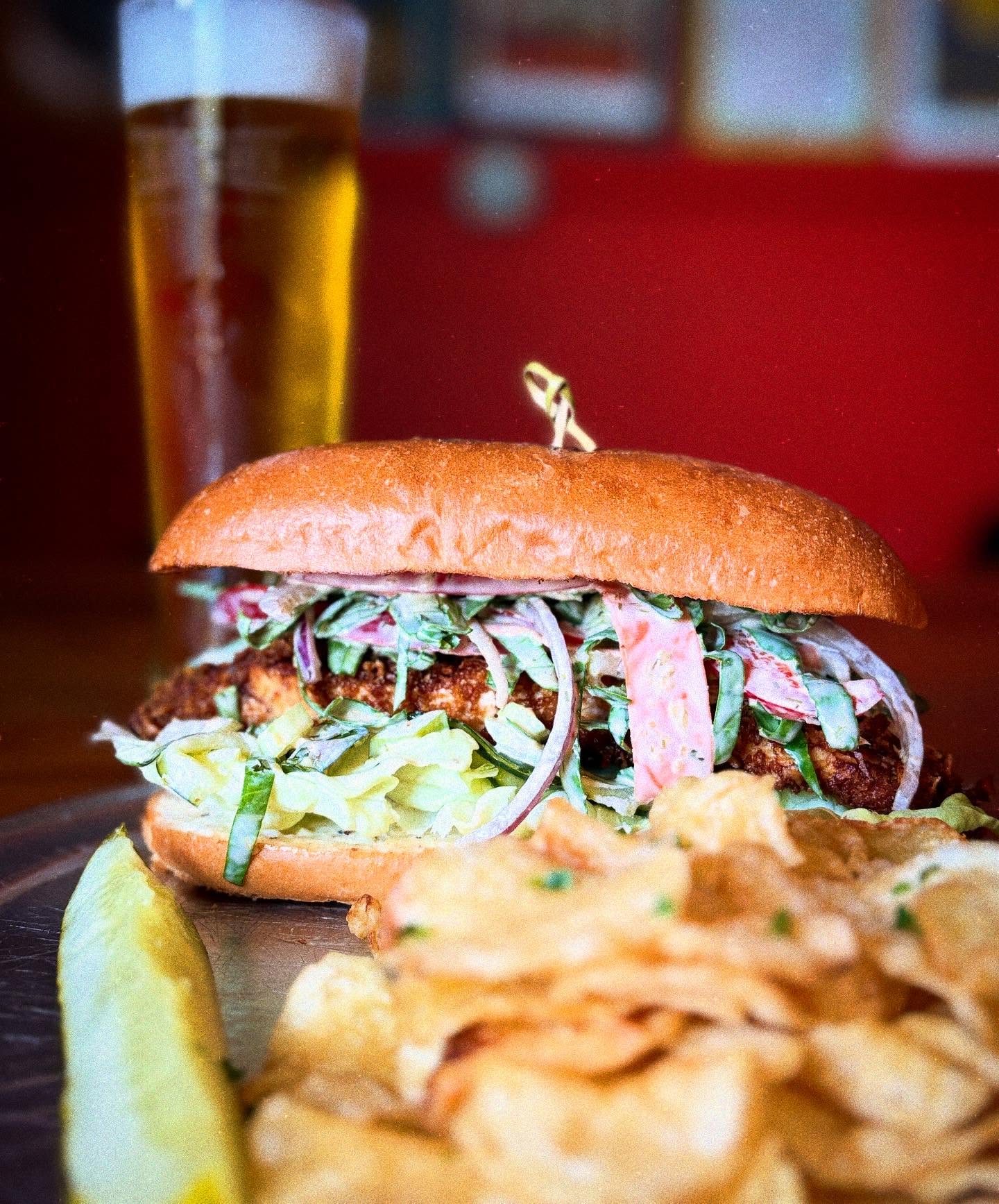 Fried chicken sandwich with coleslaw, chips, pickle, and beer.