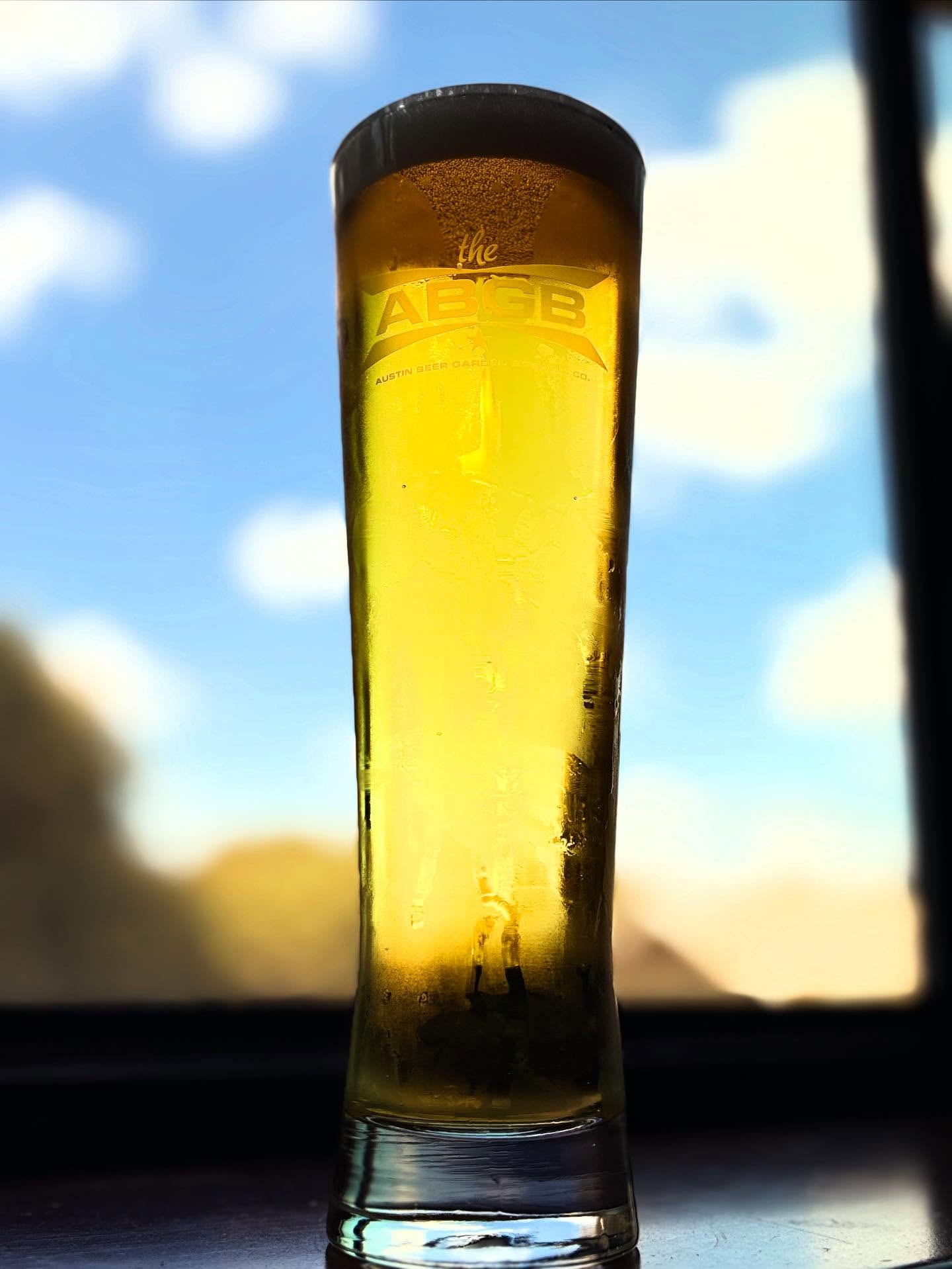 Condensation on glass of beer with AGBG logo, blue sky background.