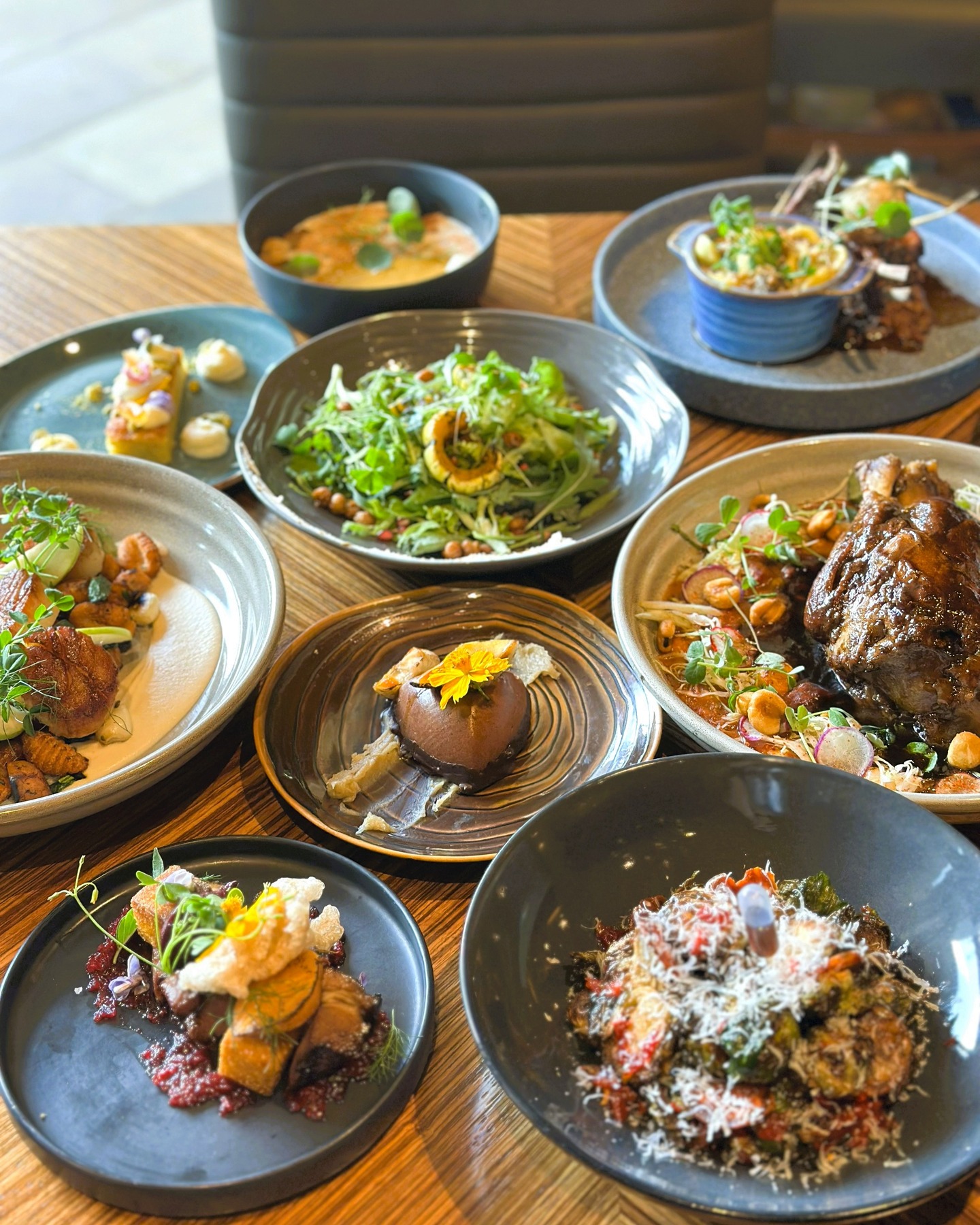 Nine plates of gourmet food arranged on a wooden table.