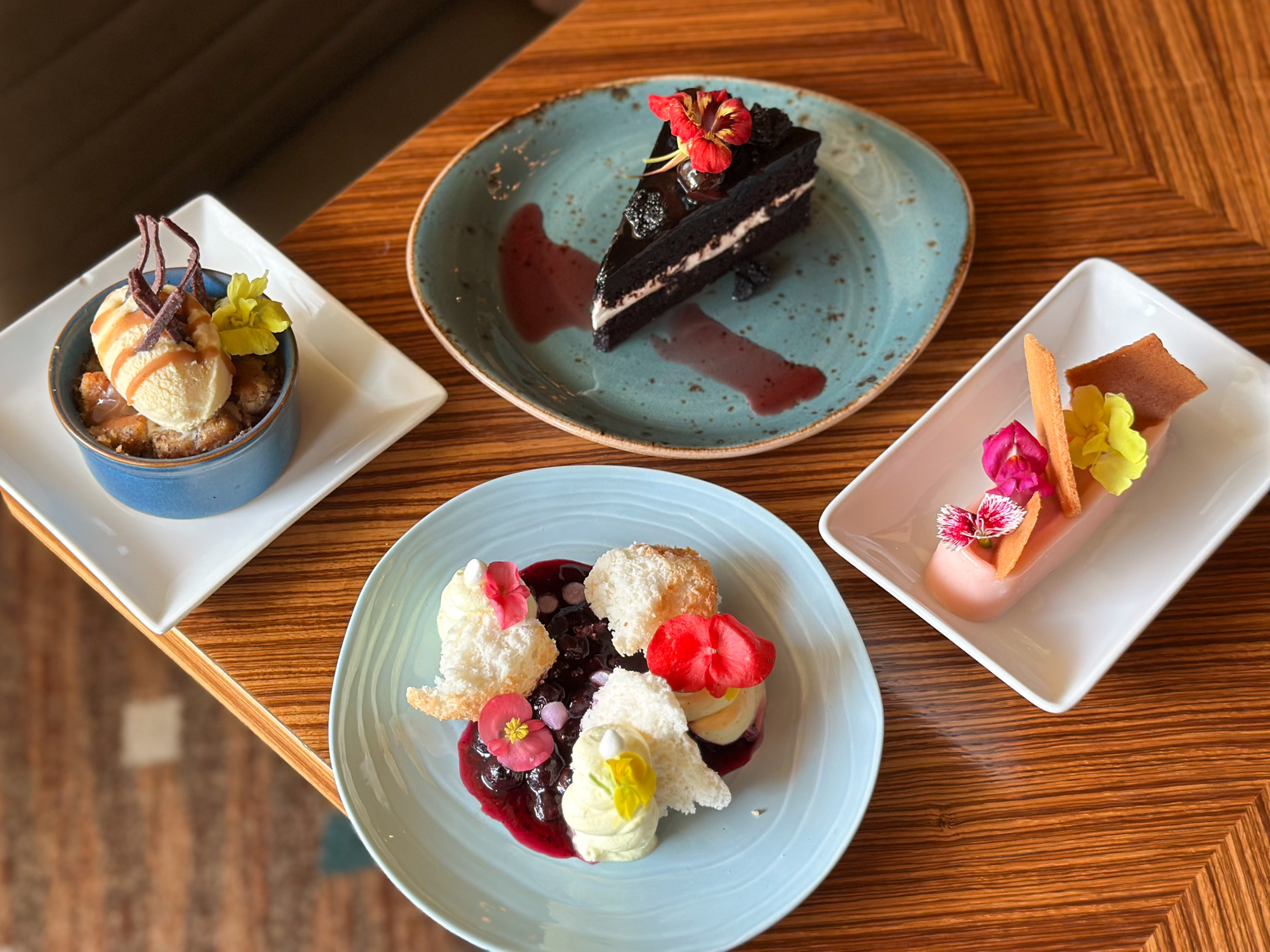 Four distinct desserts with floral garnishes arranged on a wooden table.