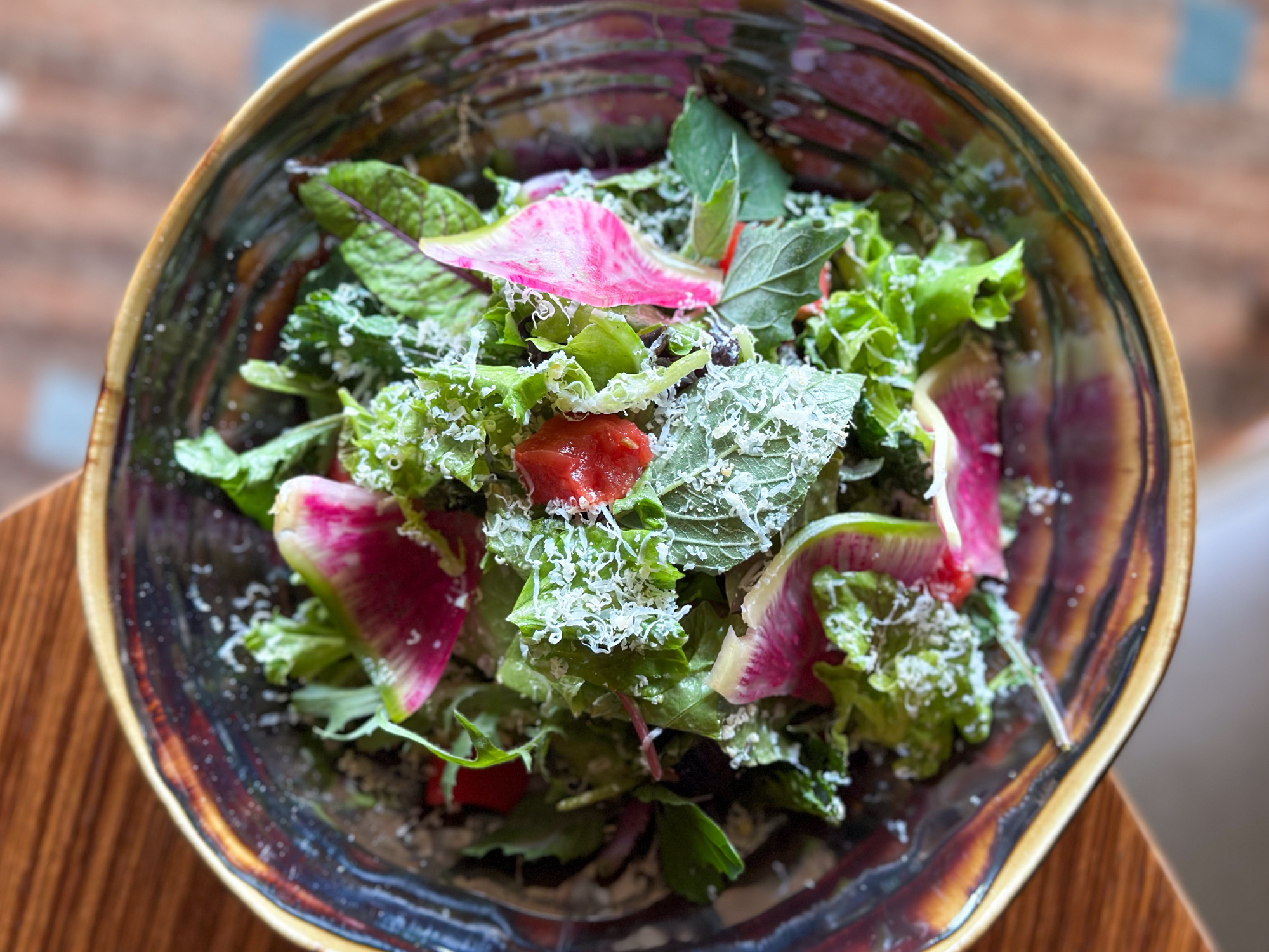 Mixed green salad with shaved cheese, watermelon radish, and red pieces.