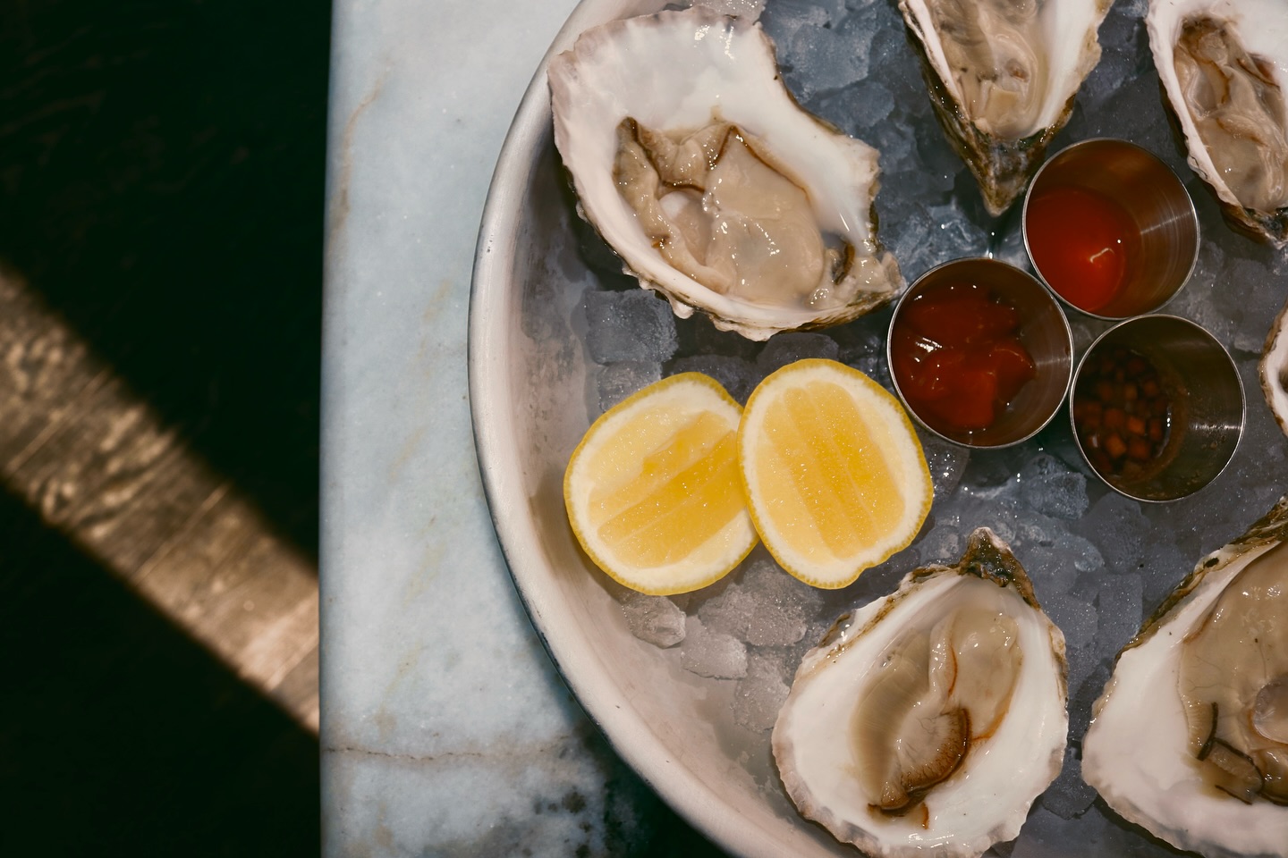 Fresh oysters on ice with lemon slices and three dipping sauces.
