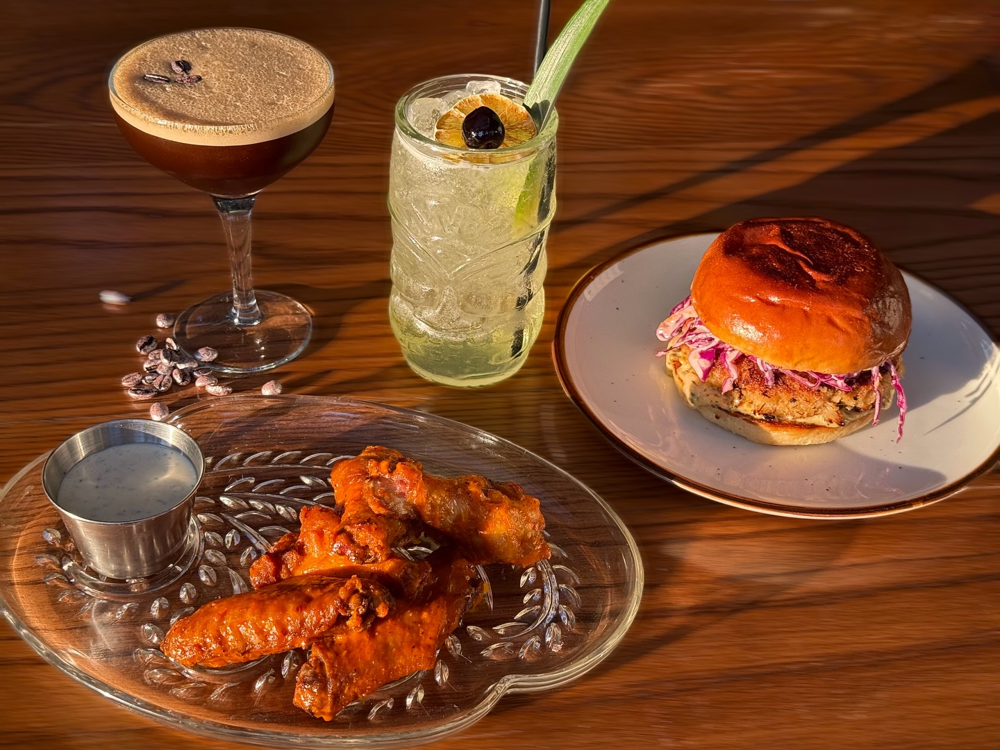 Espresso martini, cocktail, burger, and chicken wings on a wooden table.