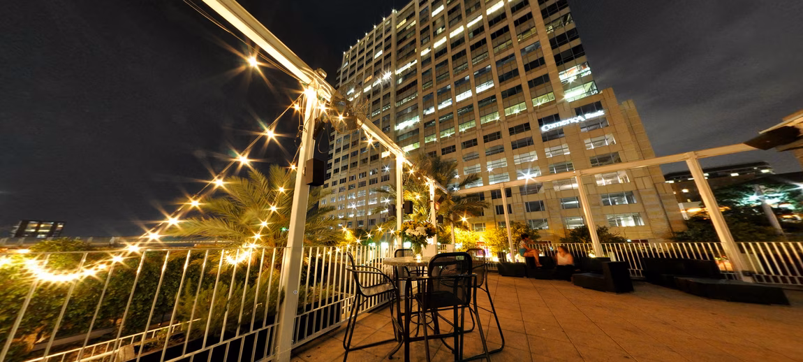 Nighttime rooftop patio with string lights, palm trees, and Comerica Bank.