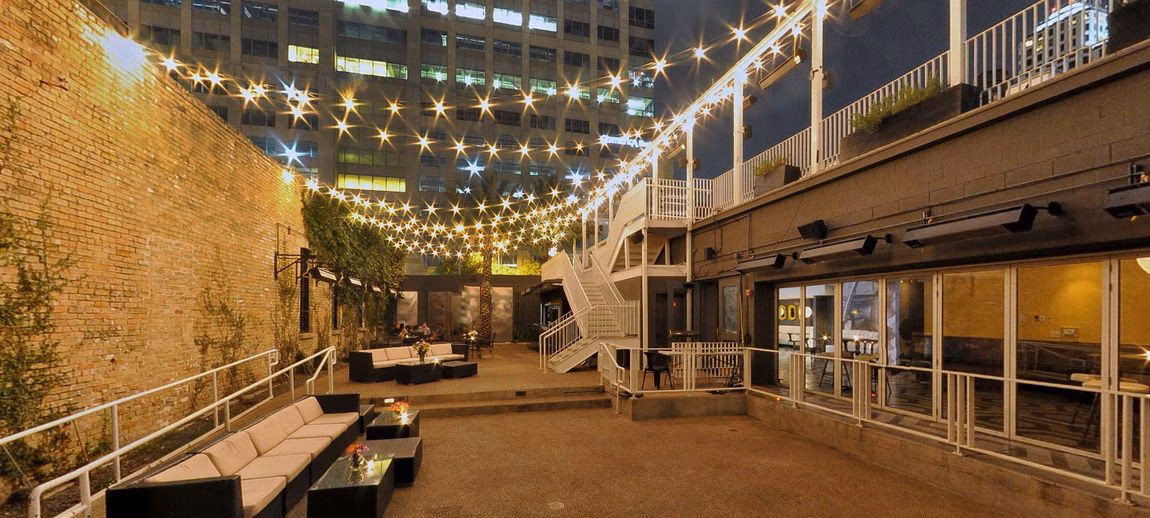 Lit outdoor patio with lounge furniture, string lights, and a brick wall.