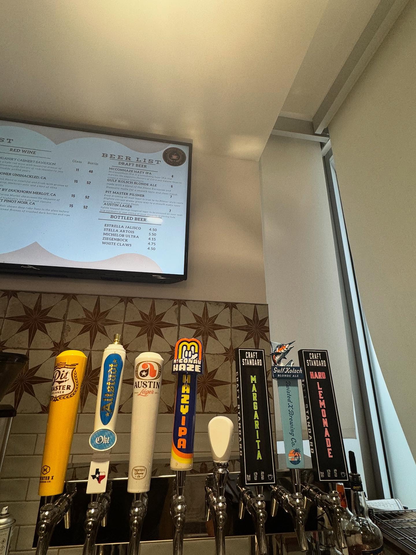 Beer tap handles line a bar below a digital menu board.