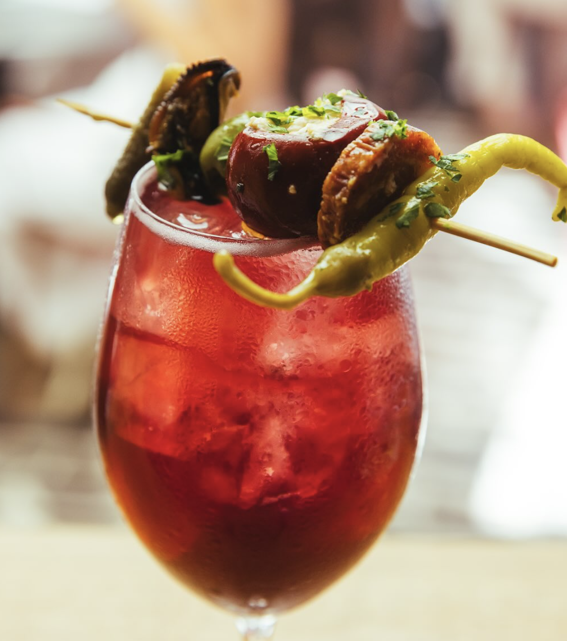 Red drink with a skewer of stuffed pepper, olive, chorizo, and mussel.