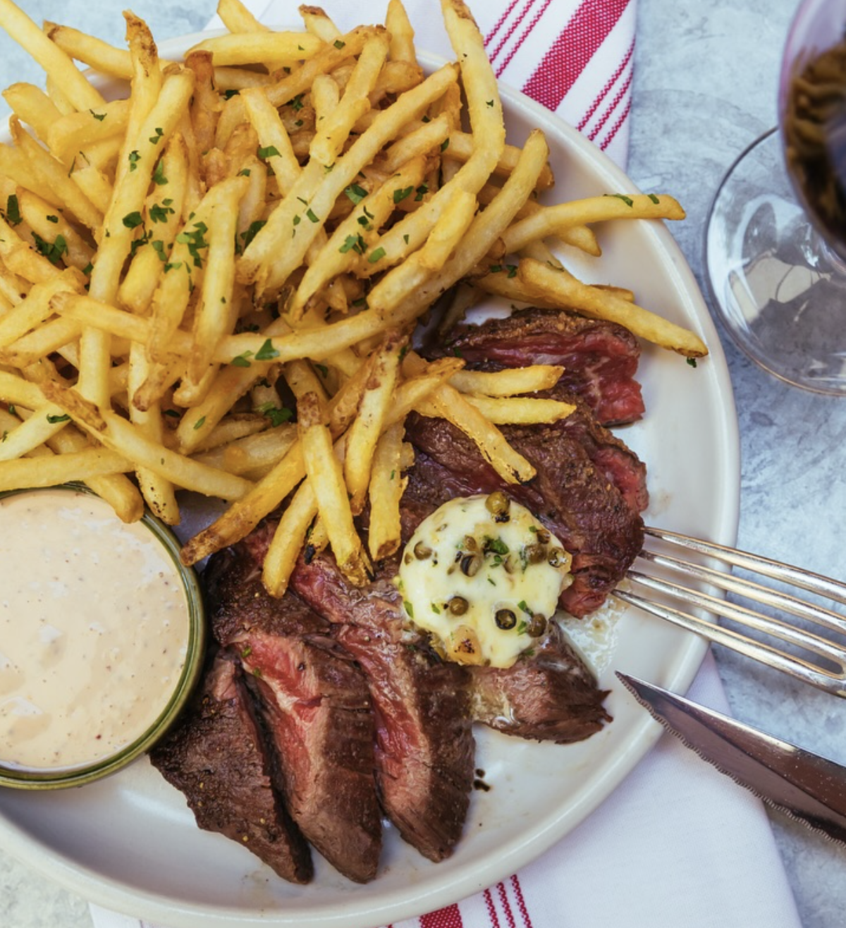 Plate of medium-rare steak, french fries, sauce, and herb butter.