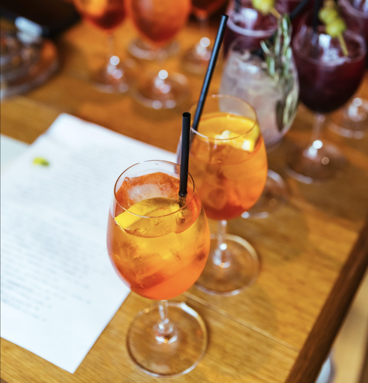 Multiple drinks with ice and garnishes on a wooden table.