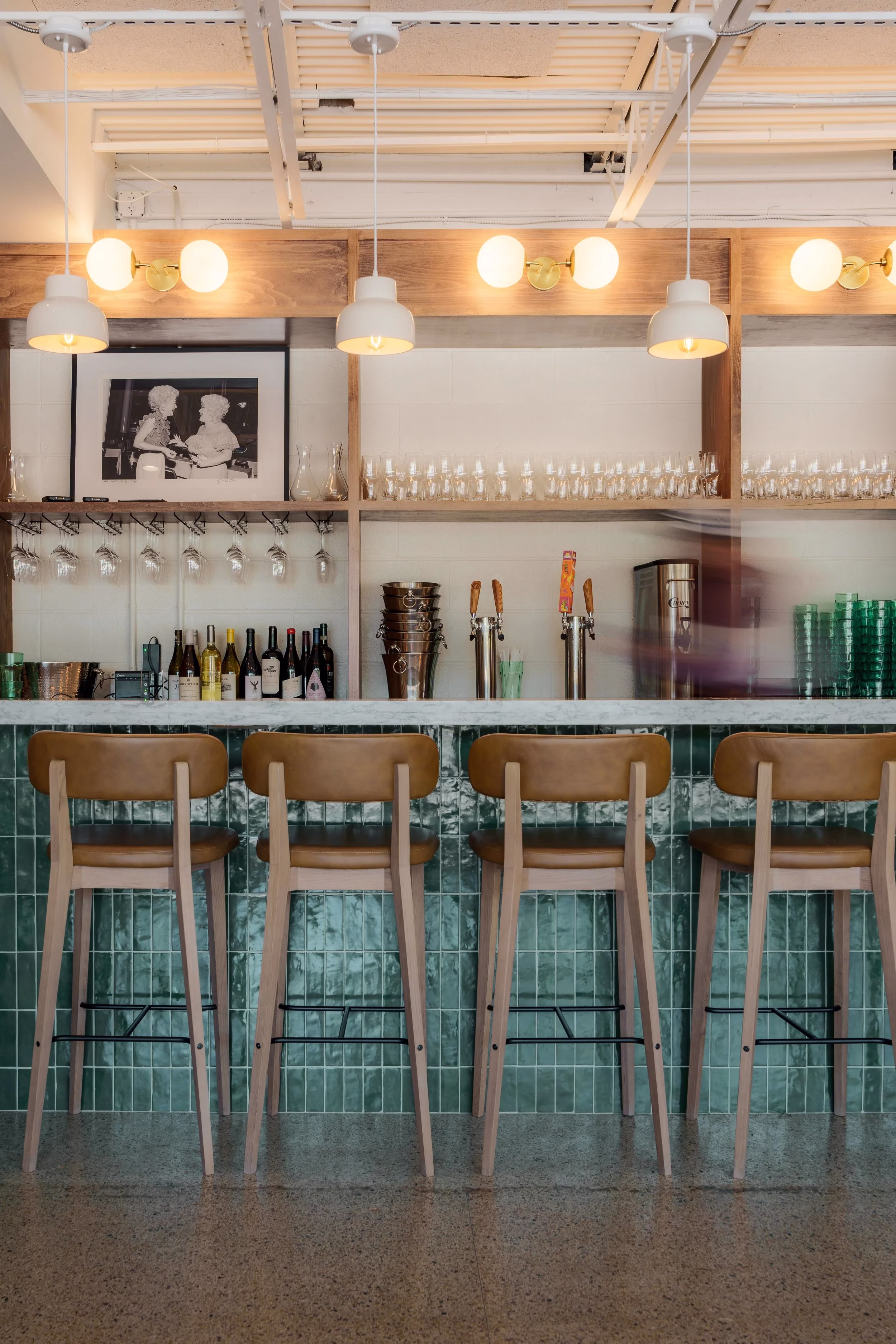 Bar with green tile, wooden shelves, marble counter, and leather stools.
