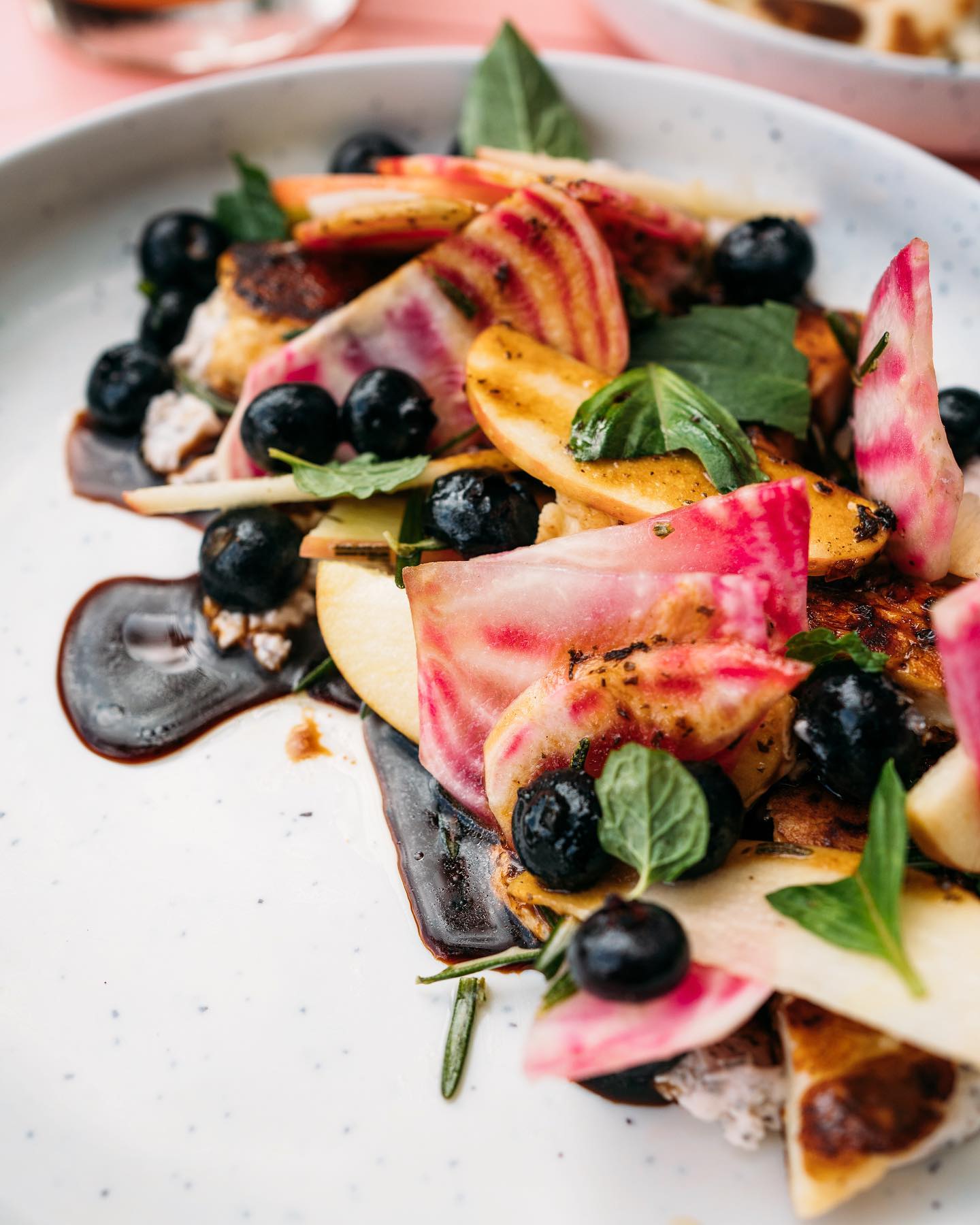 Colorful dish featuring blueberries, striped beets, seared fruit, and fresh herbs.
