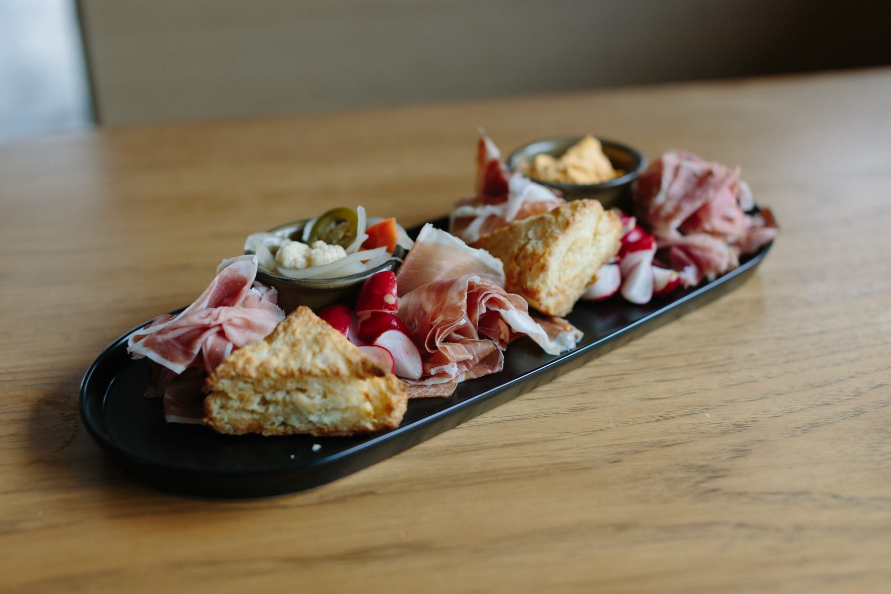 Platter of sliced ham, scones, radishes, pickled vegetables, and dip.