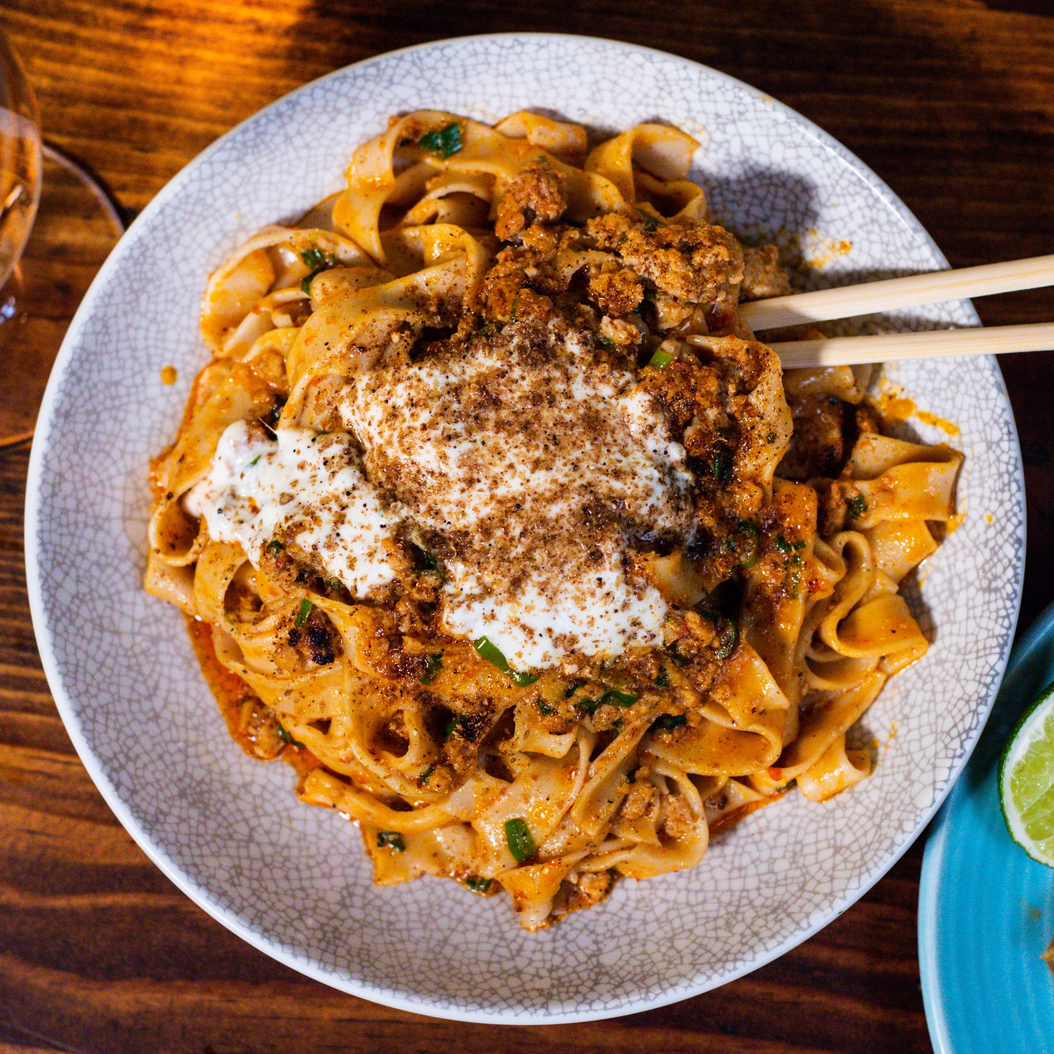 Bowl of wide noodles with meat, creamy topping, and chopsticks.