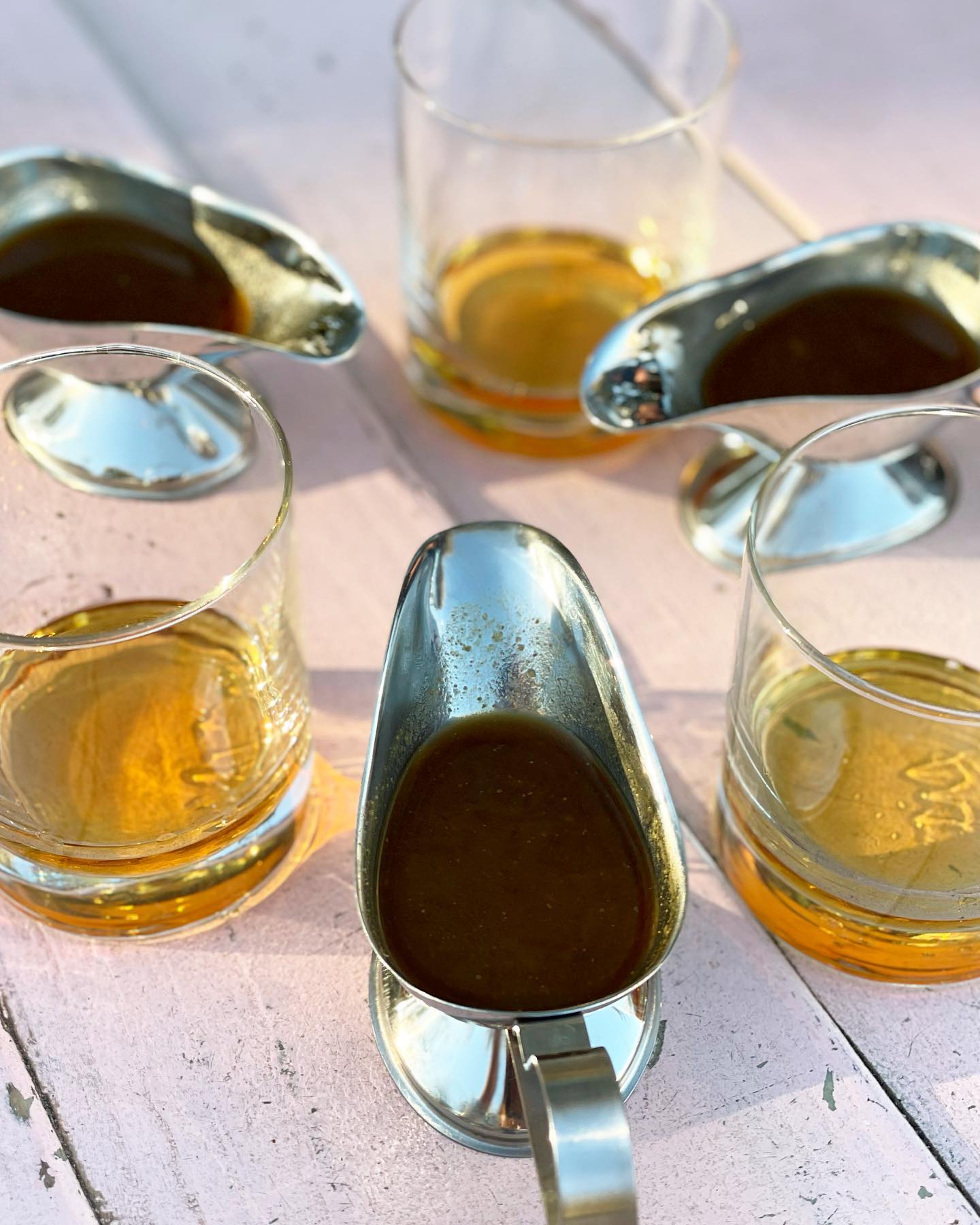 Three gravy boats with brown liquid, three glasses with amber liquid.