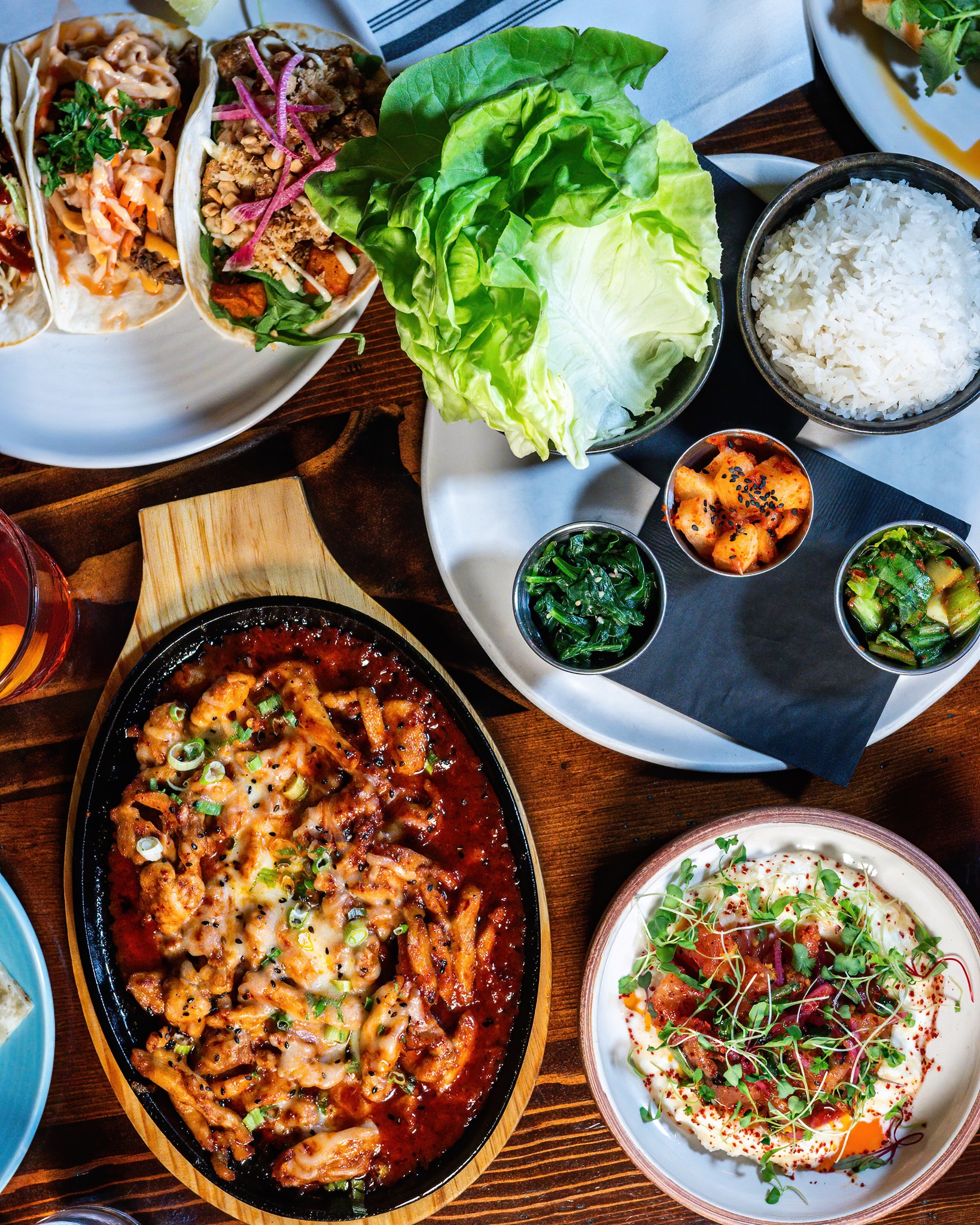 Top-down view of a Korean food spread with tacos and sizzling chicken.