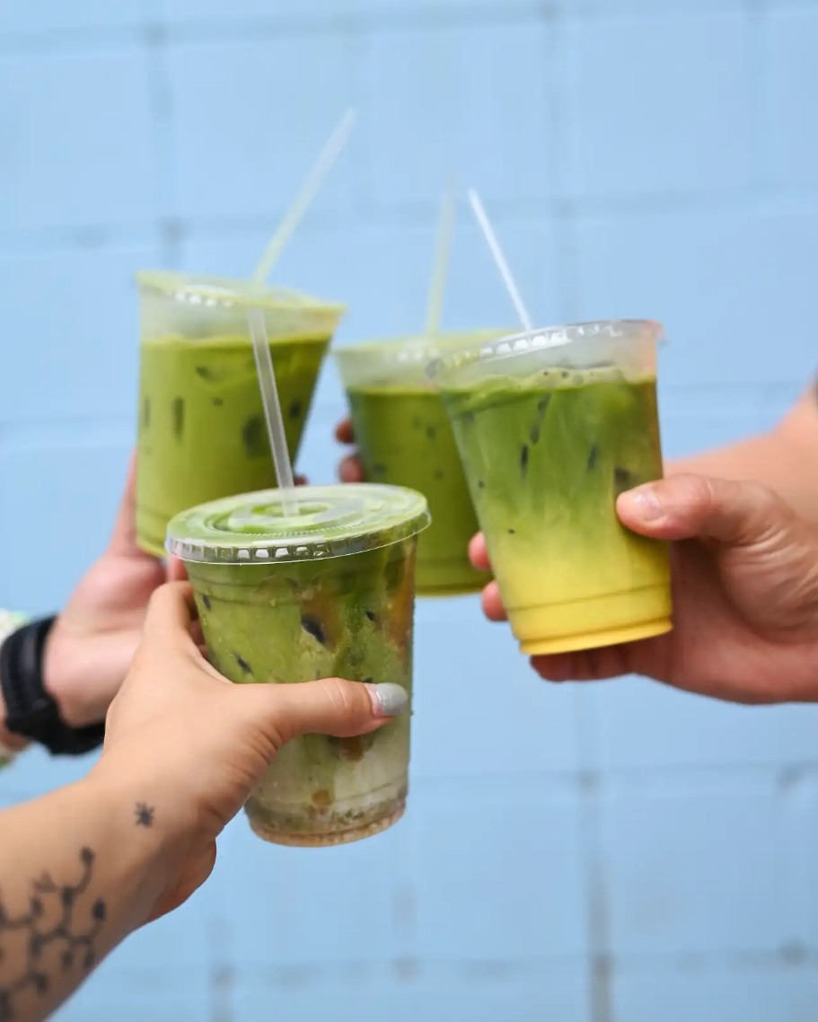 Four hands hold green layered drinks in clear cups with straws.
