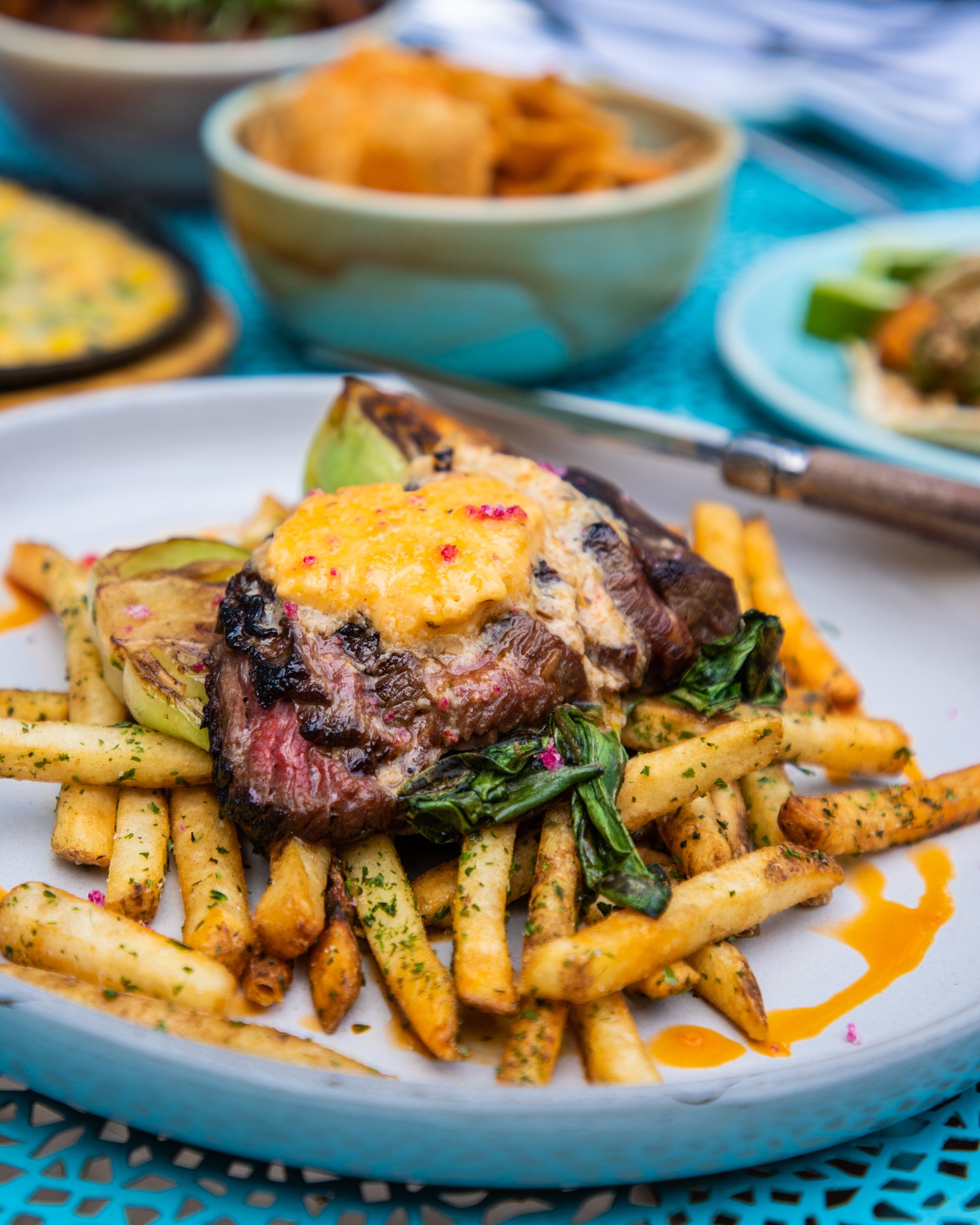 Grilled steak, fries, greens, and yellow sauce on a white plate.
