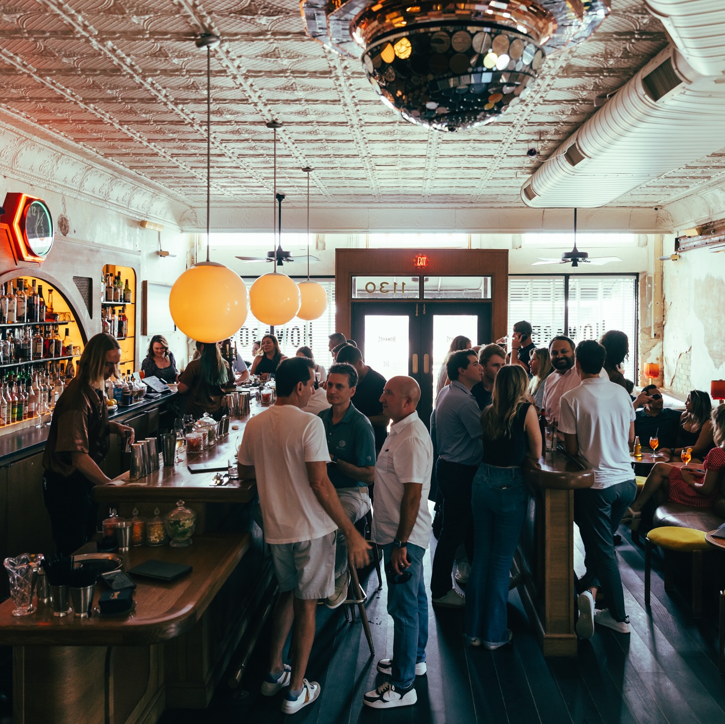 People socializing at a busy bar with a bartender and disco ball.