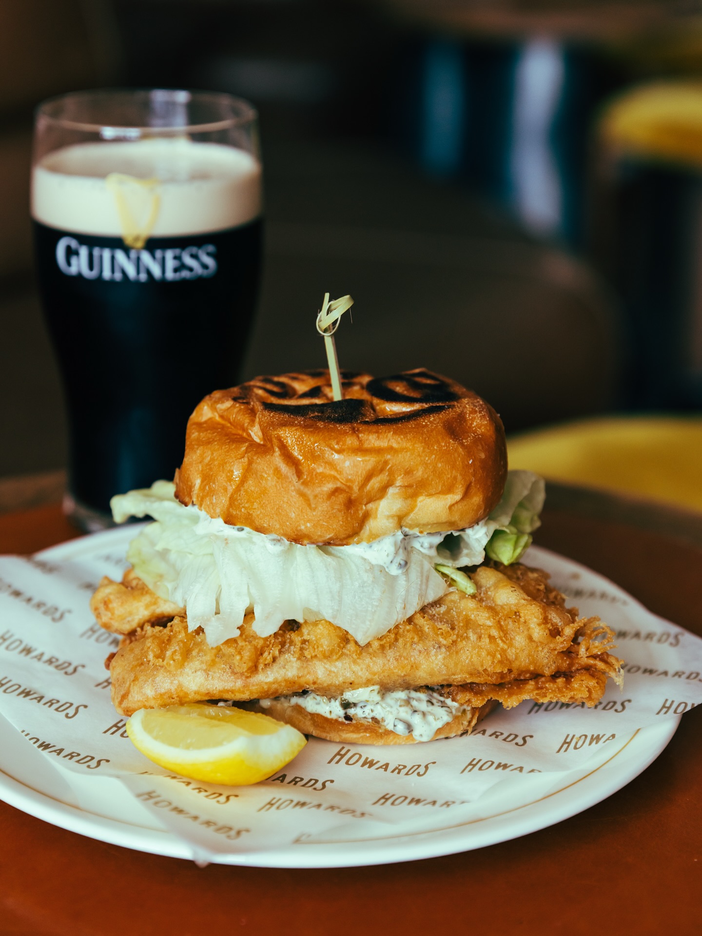 Fish burger with lettuce, tartar sauce, lemon, and Guinness beer.