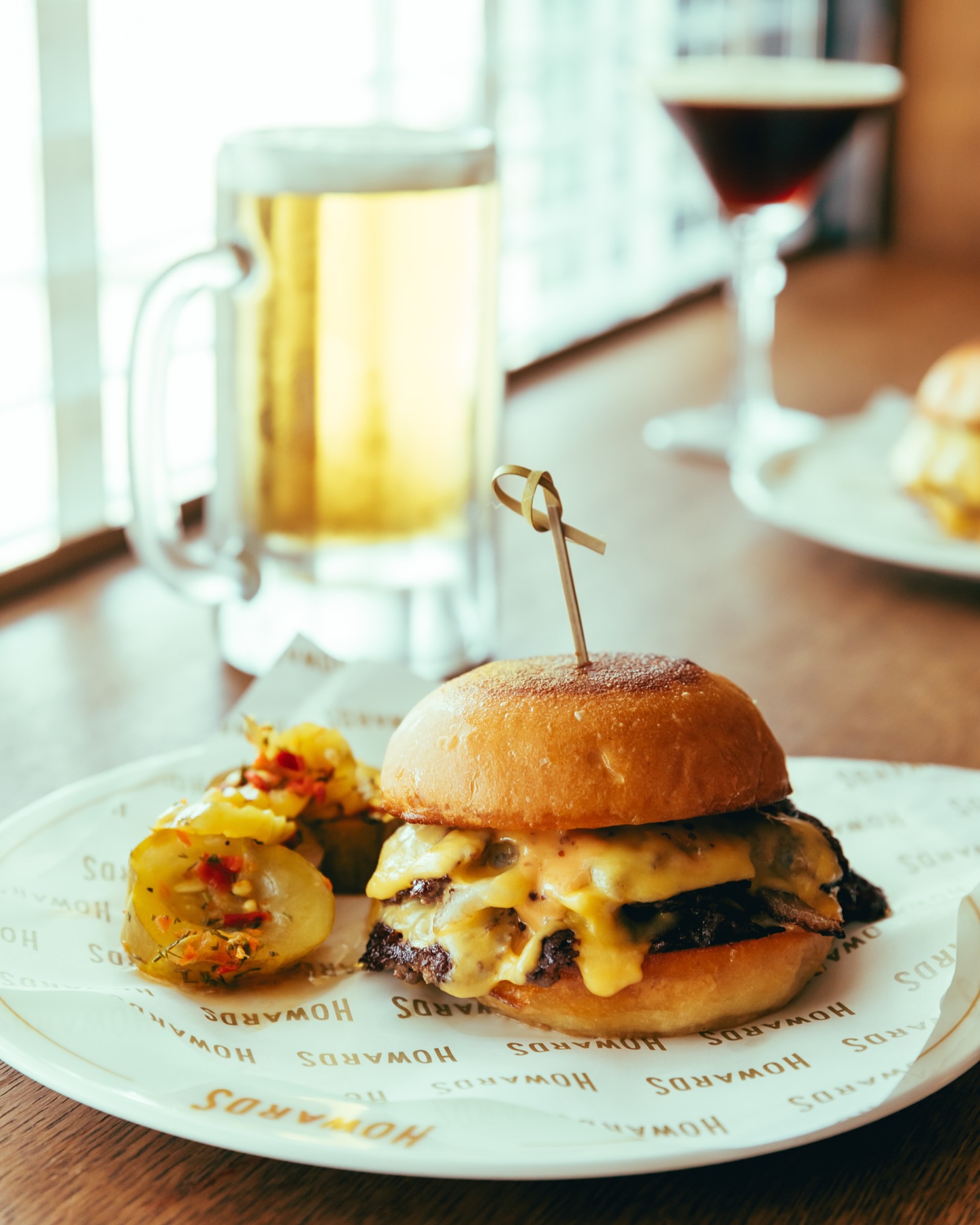 A cheeseburger with pickles, a beer, and a cocktail.