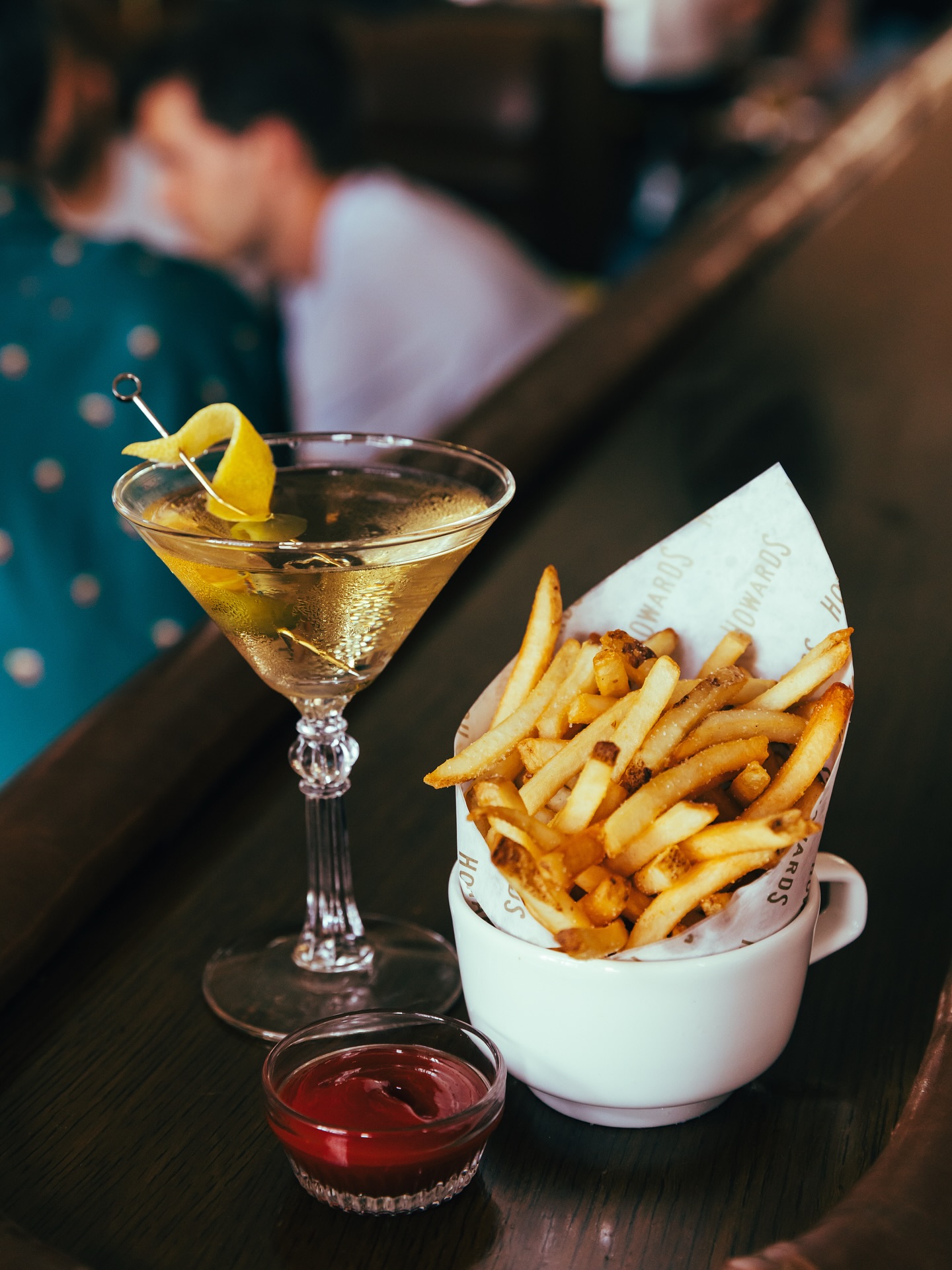 Martini with lemon twist, french fries, and ketchup on a bar.
