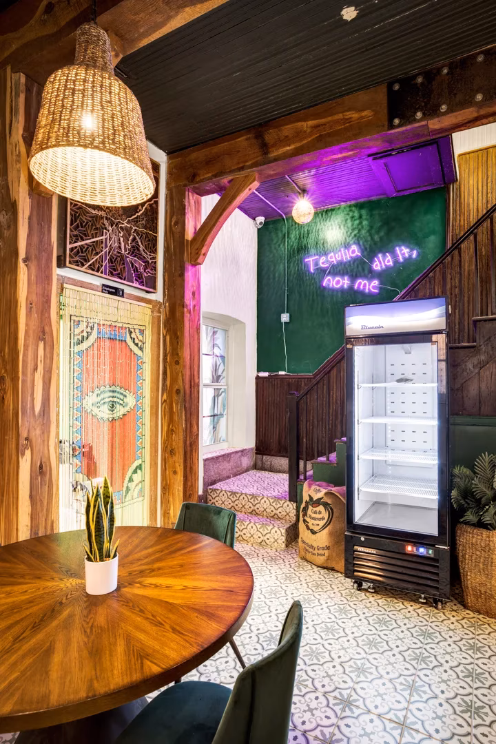 Interior with 'Tequila did it' neon sign, woven lamp, and wooden table.