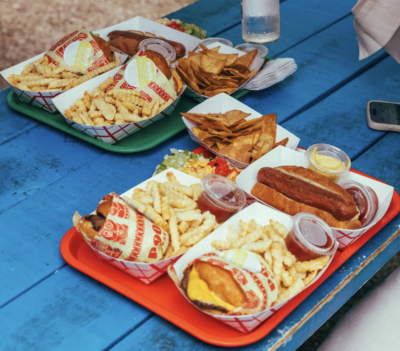 Multiple trays of hot dogs, burgers, fries, and tortilla chips.