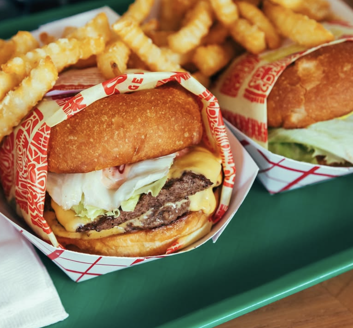 Two cheeseburgers and crinkle-cut fries on a green tray.