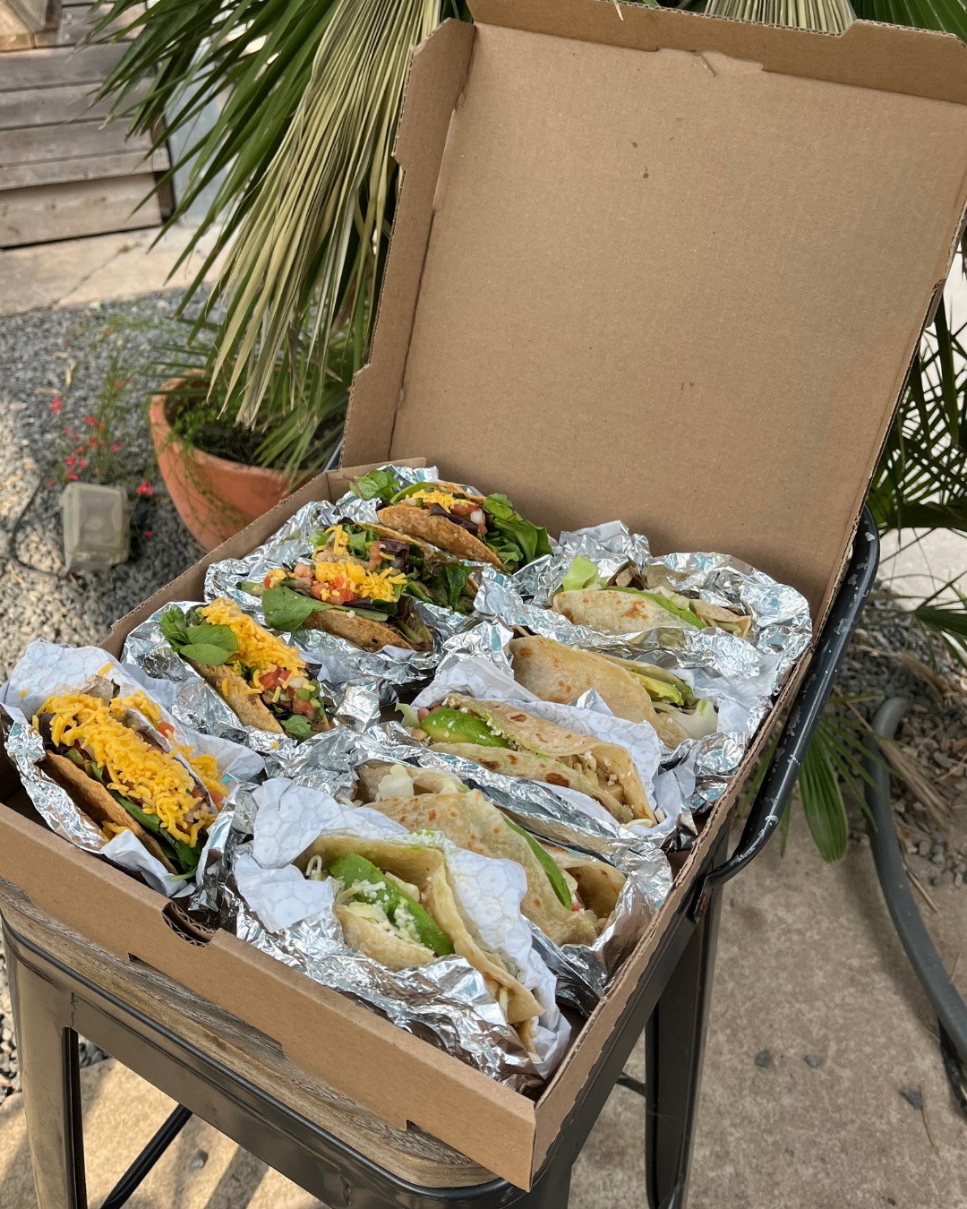 Numerous tacos in foil, arranged in an open cardboard box.