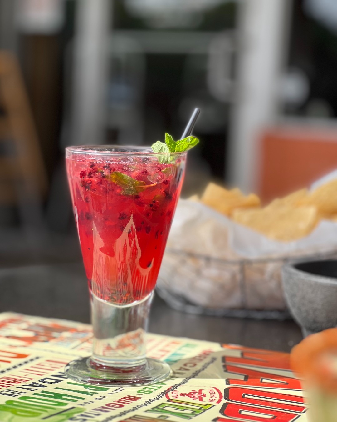 Tall glass of a red drink with berries and mint garnish.